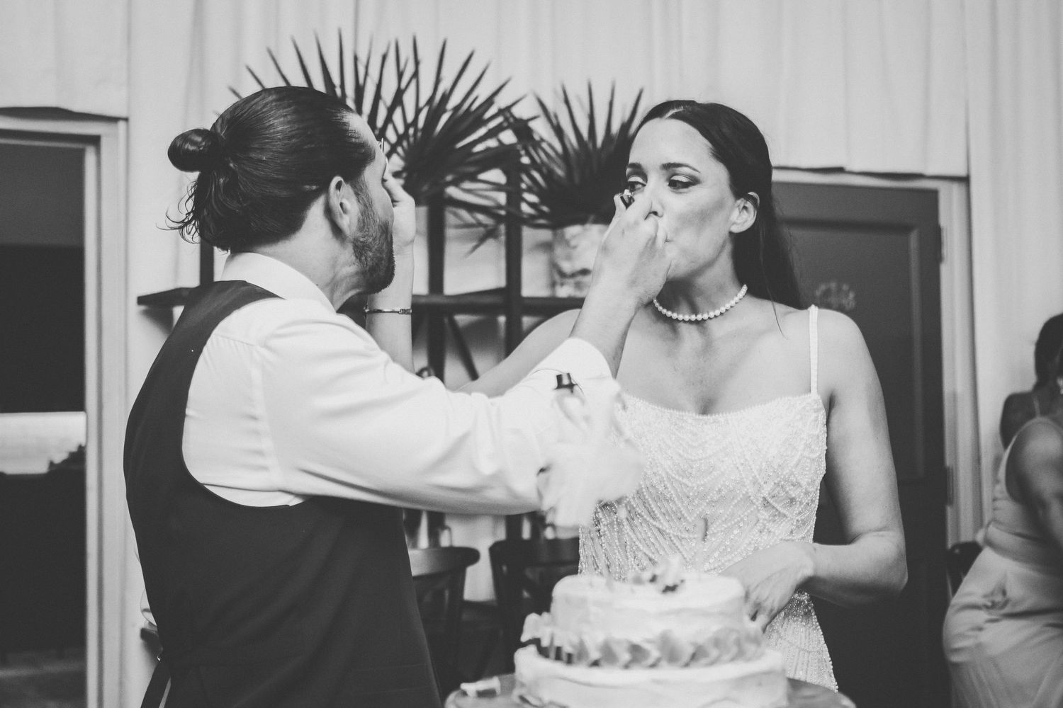 Black and white photo of bride and groom sharing cake cutting moment at wedding reception.