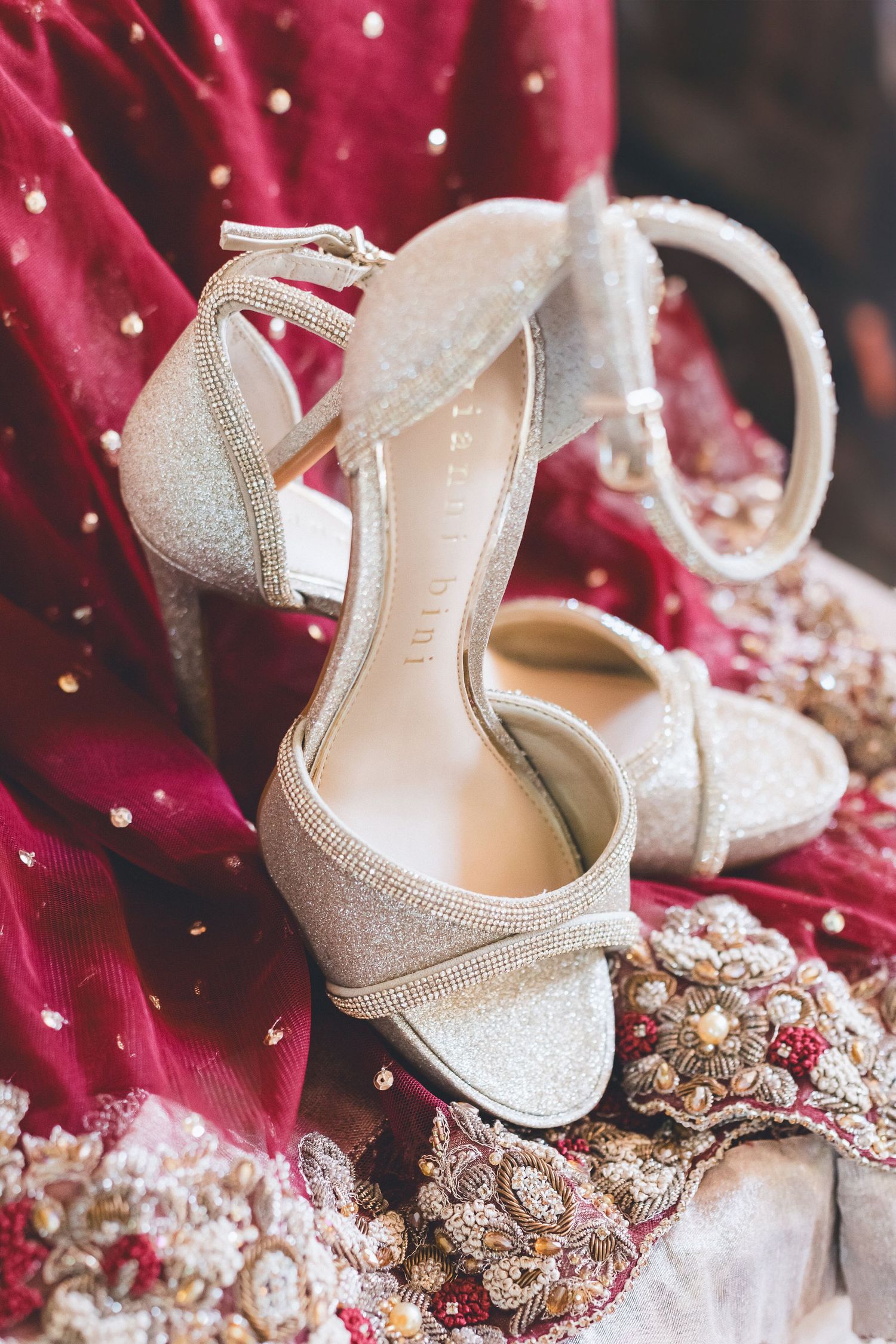 Sparkling silver block heel bridal sandals resting on red embroidered South Asian wedding dress fabric.