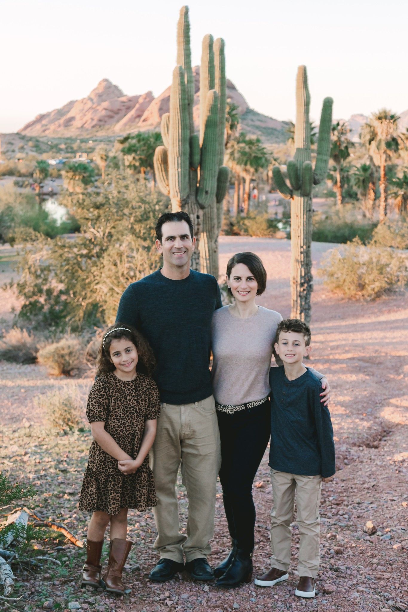Family of four poses before tall saguaro cacti with Camelback Mountain at sunset.