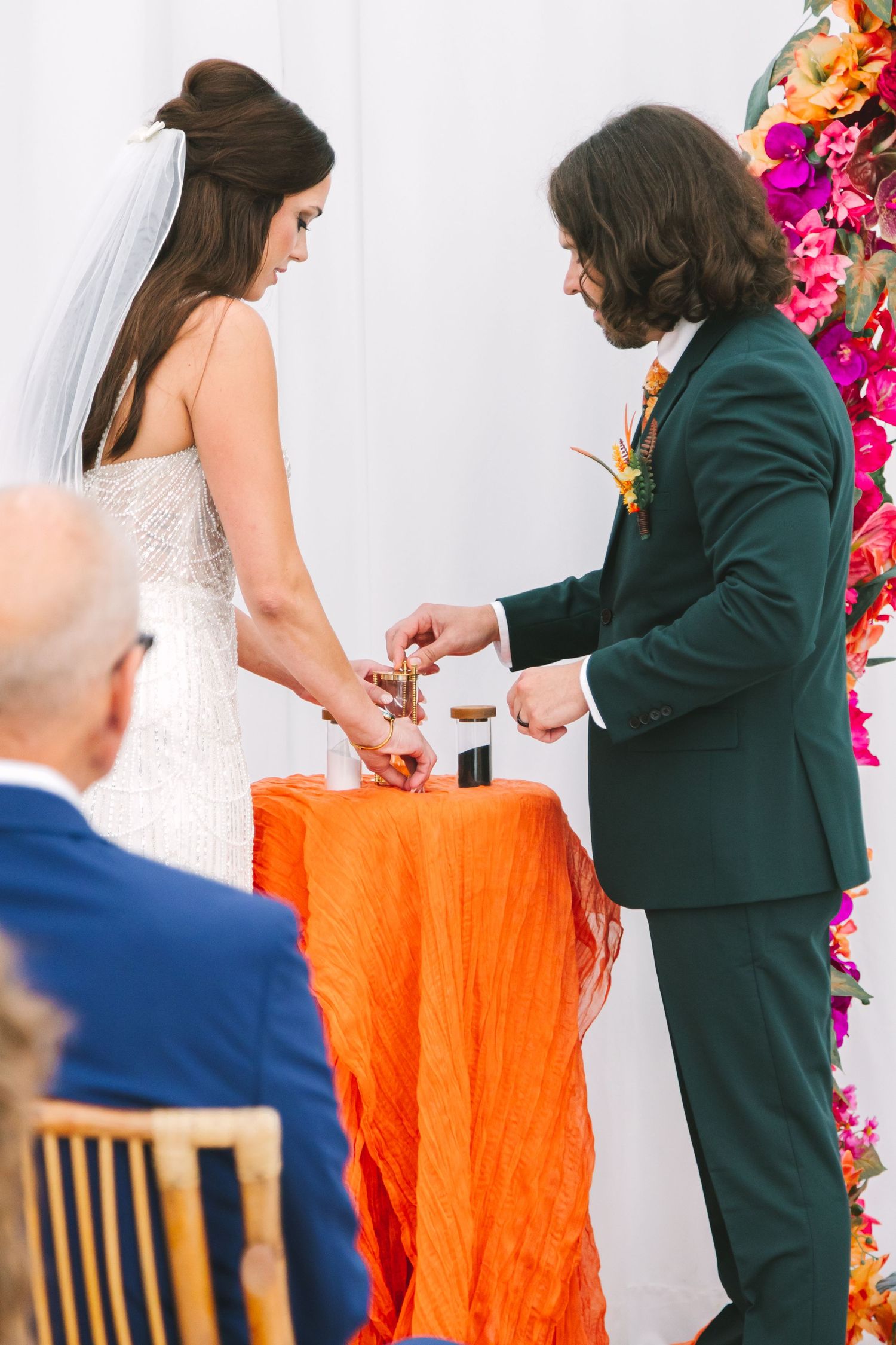 Bride and groom performing a sand unity ceremony at a colorful floral altar during their wedding.