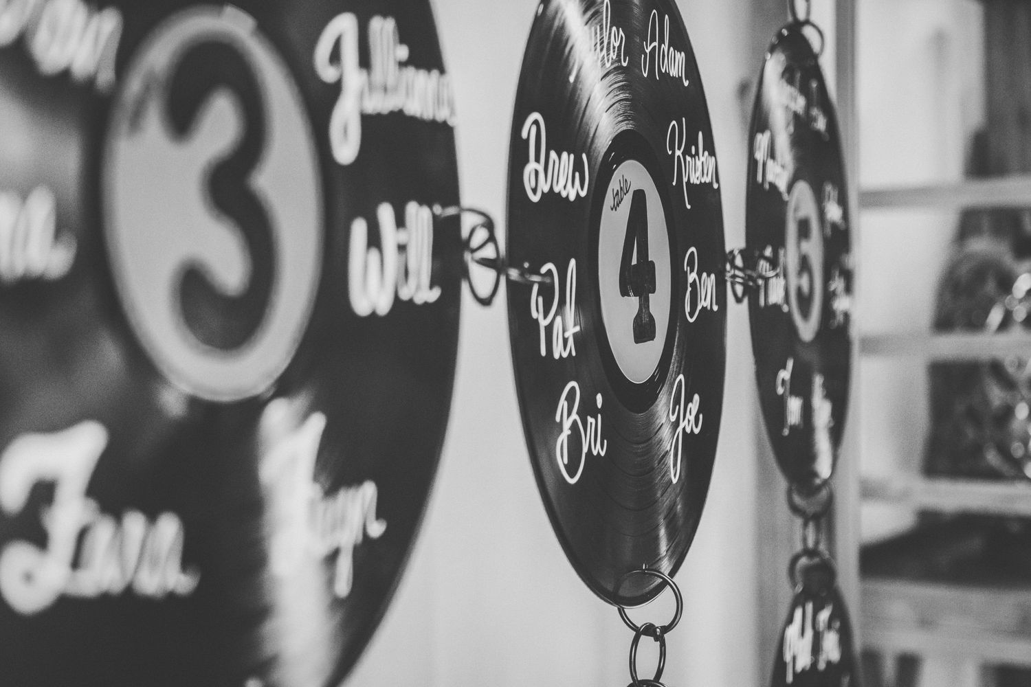 Black and white photo of vinyl records used as table number signs with handwritten names at a wedding reception.