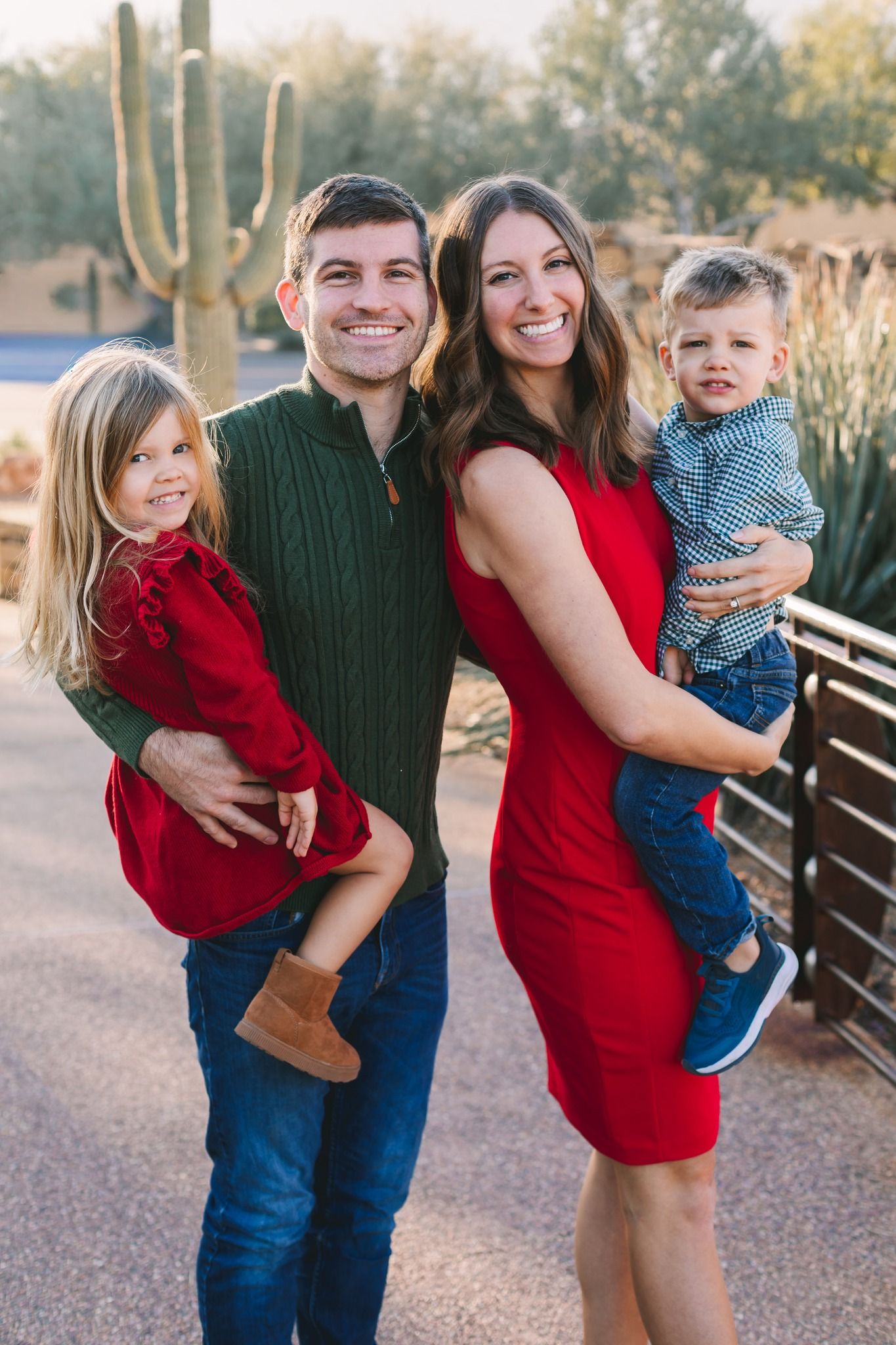 Smiling family of four with two young children posing outdoors near a cactus in warm sunlight.