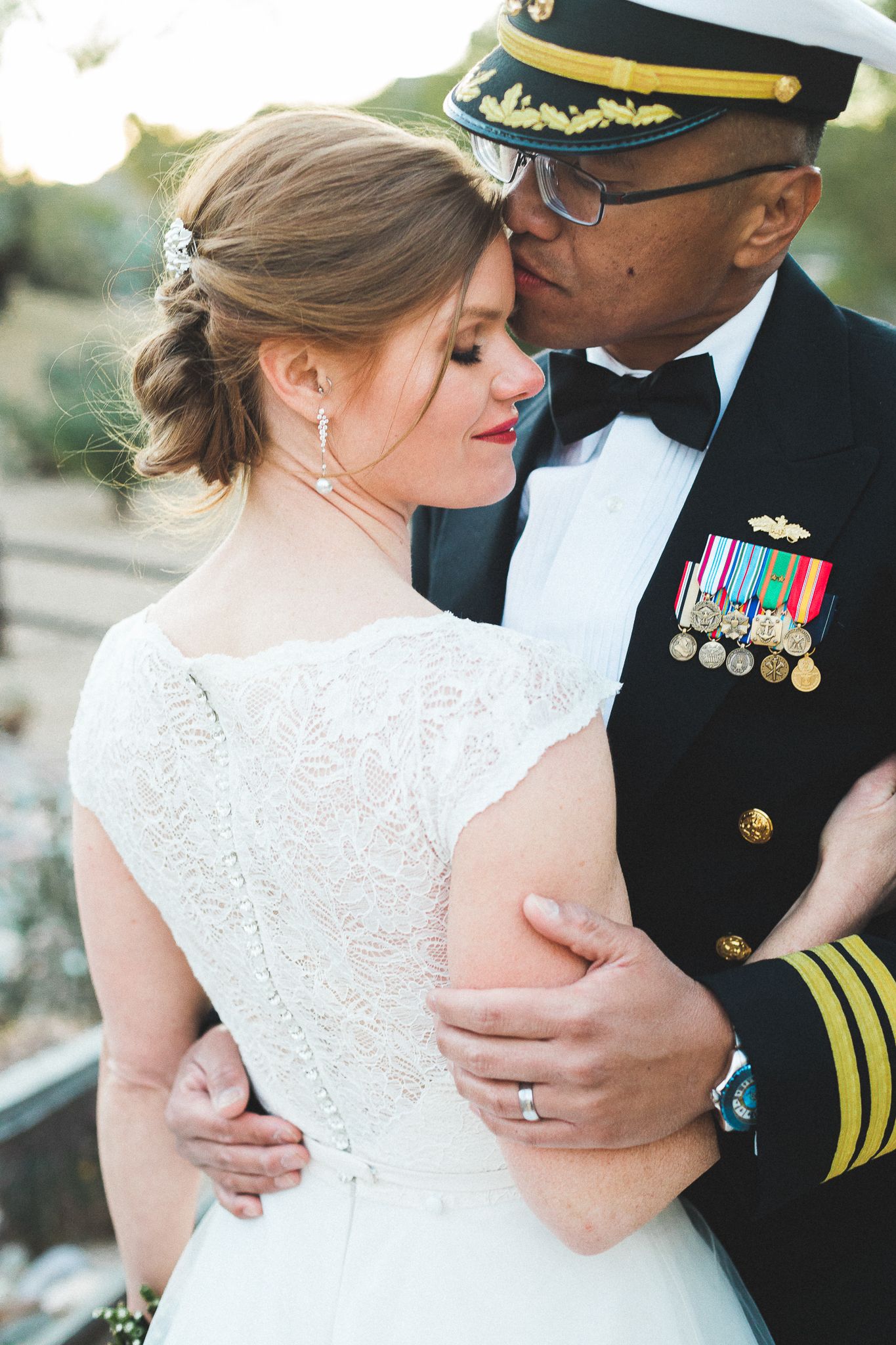 Military groom in dress uniform kissing bride on the forehead during their wedding portrait.
