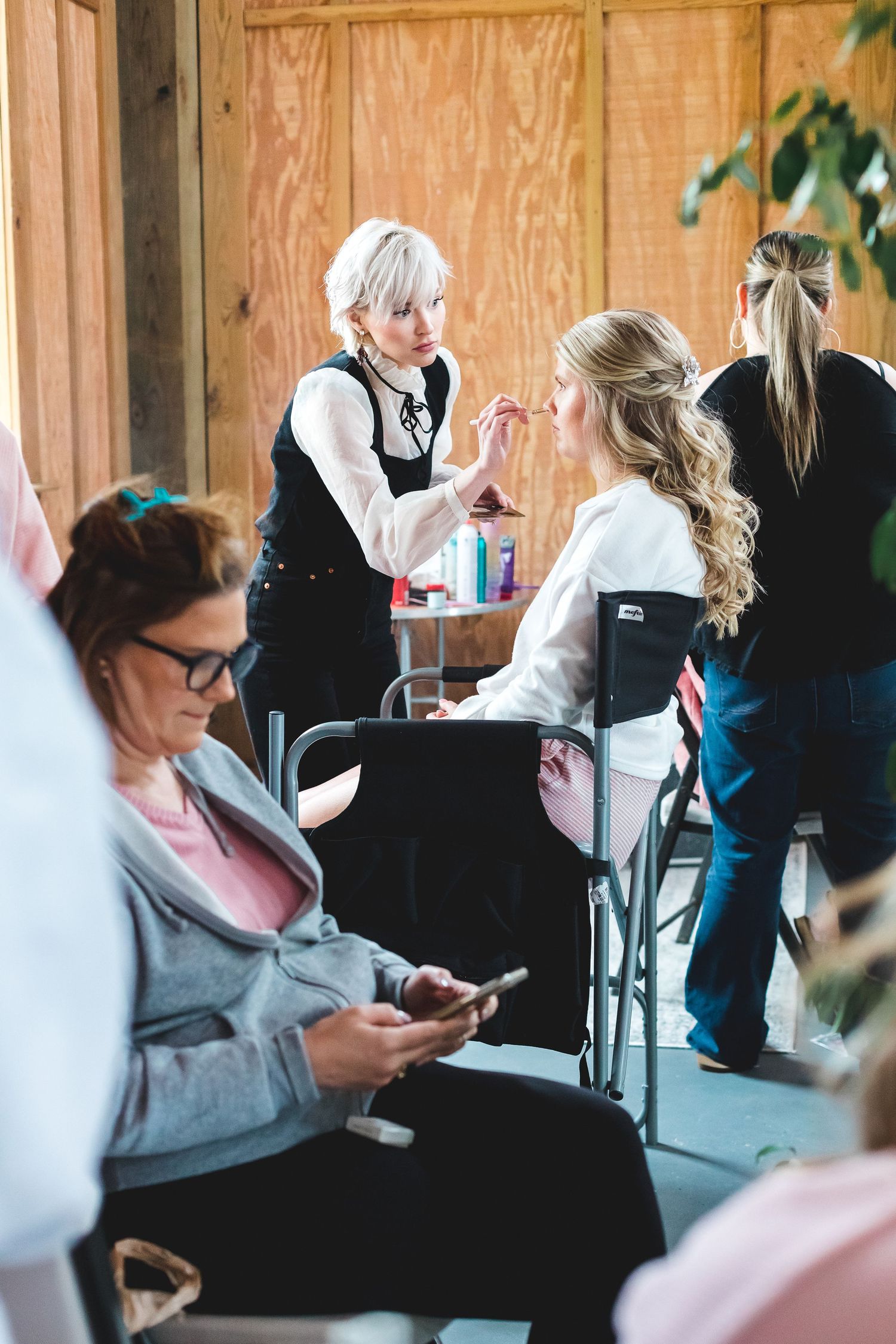 Professional makeup artist applying makeup to a bride during wedding day preparations in a rustic barn setting.