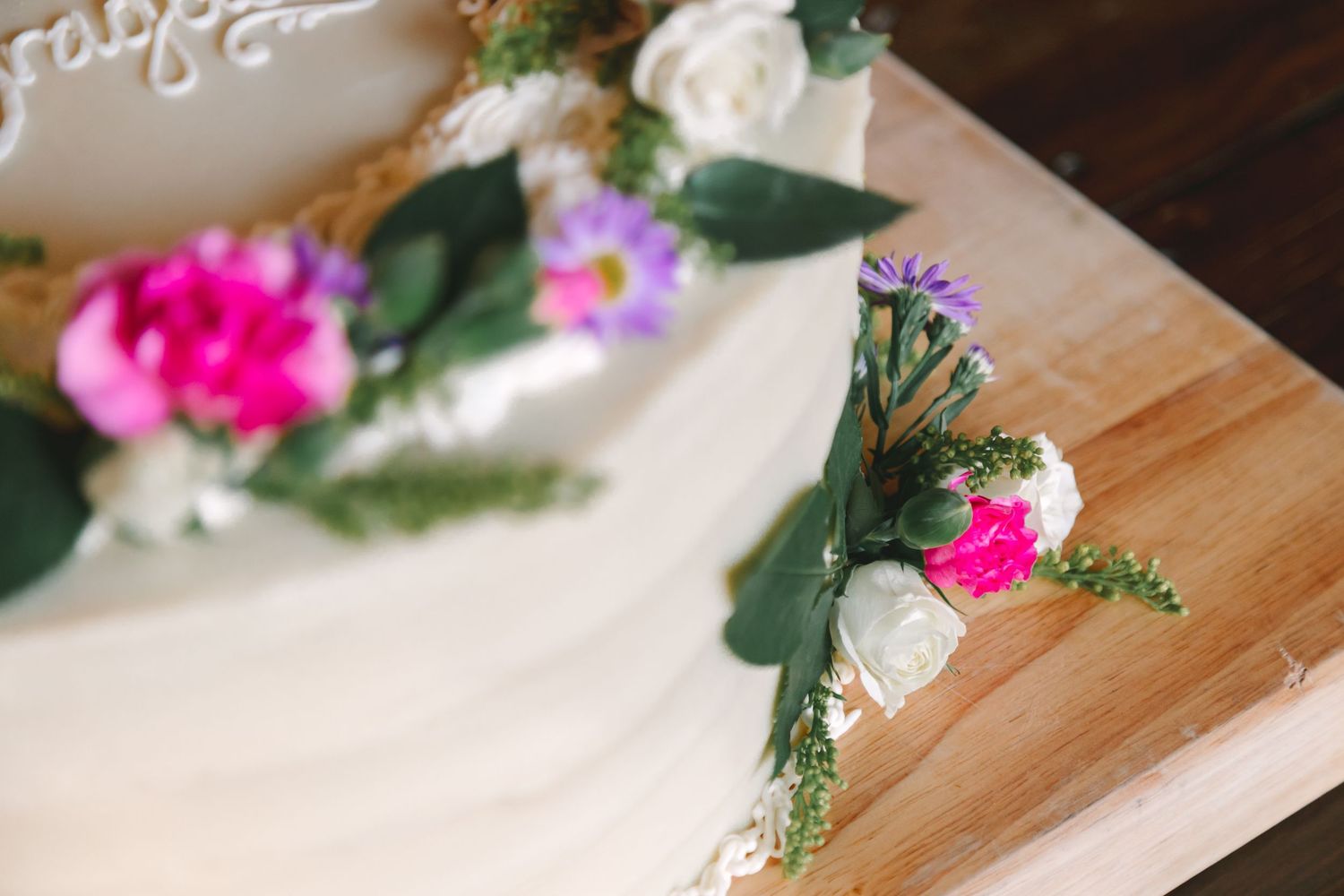 Close-up of elegant white wedding cake decorated with pink, purple, and white fresh flowers.