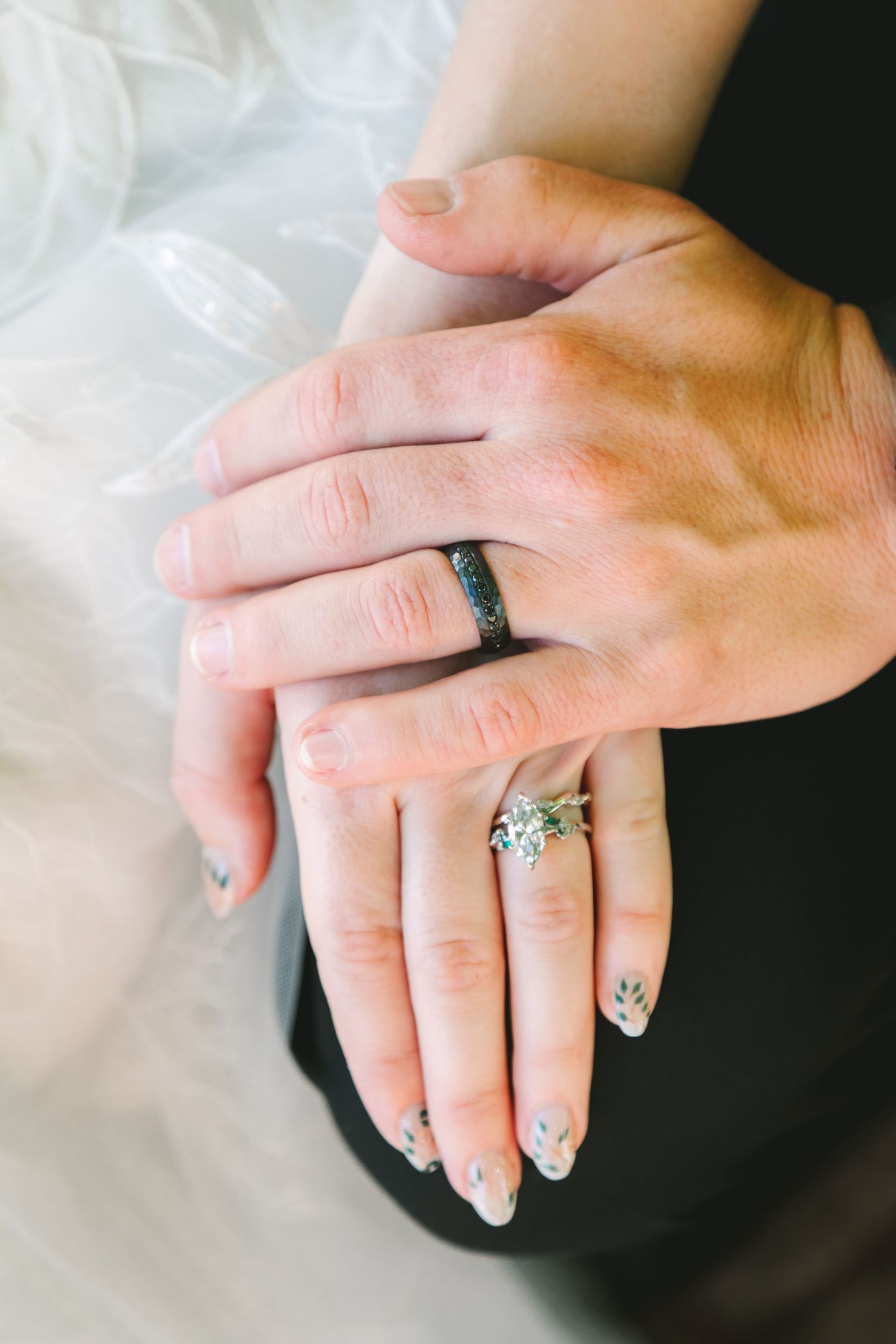 Close-up of bride and groom's hands showing diamond engagement ring and dark wedding band.