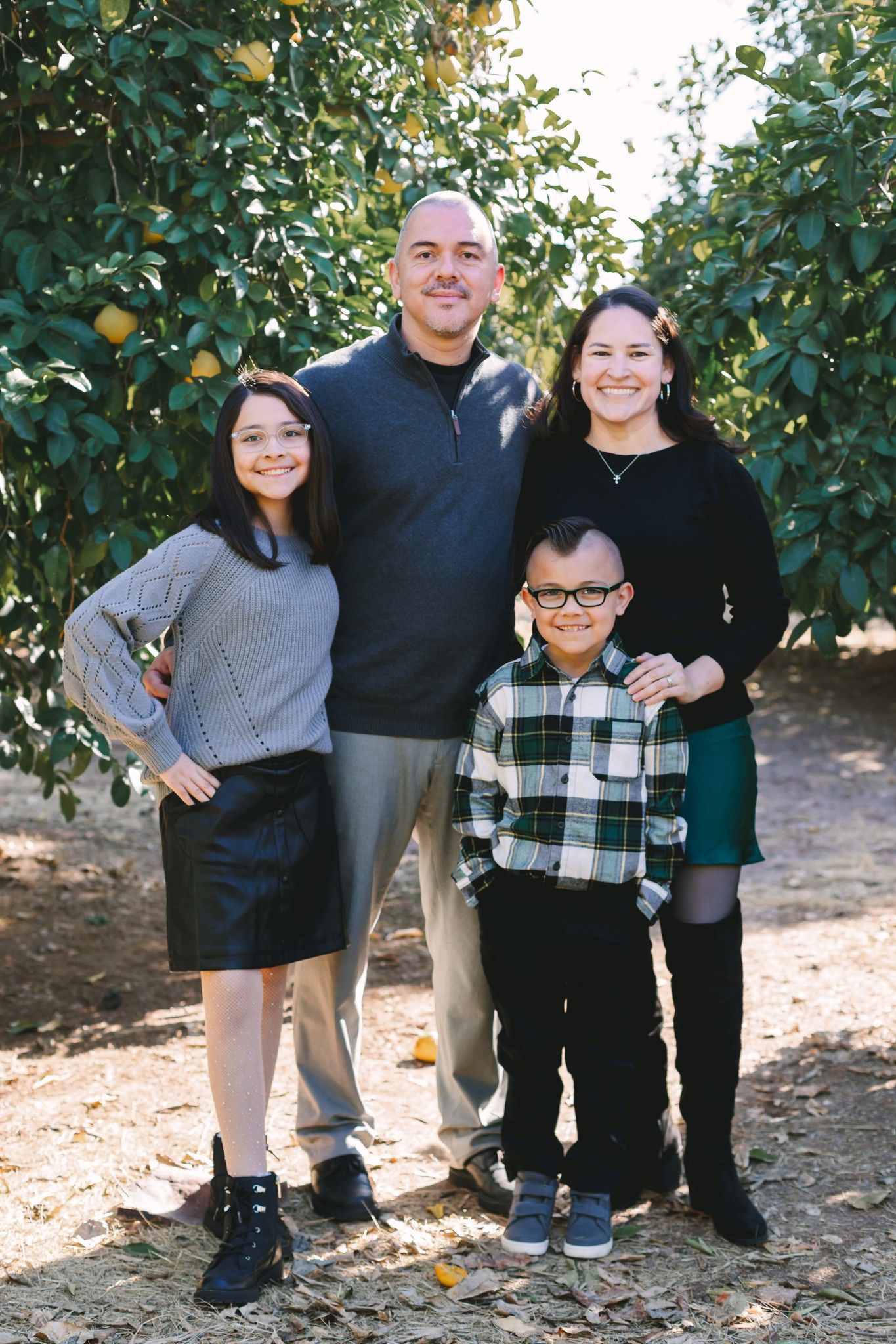 Family of four smiles together in lush citrus orchard during fall family portrait.