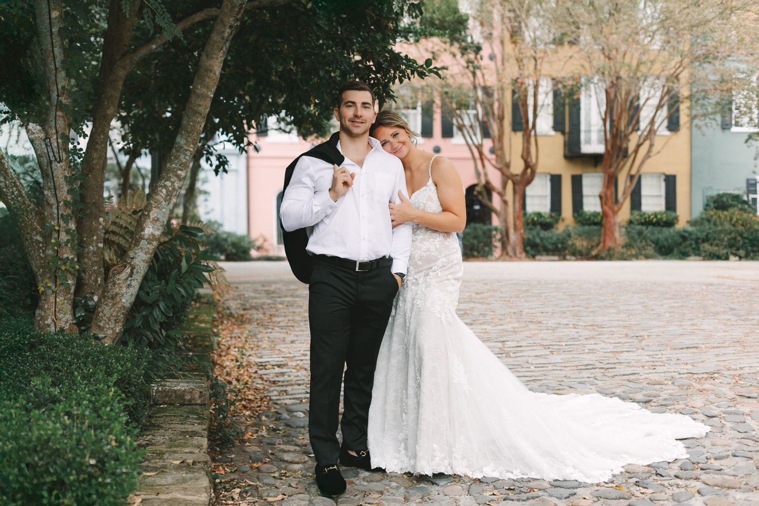 Bride and groom pose together on cobblestone street with colorful historic buildings behind.
