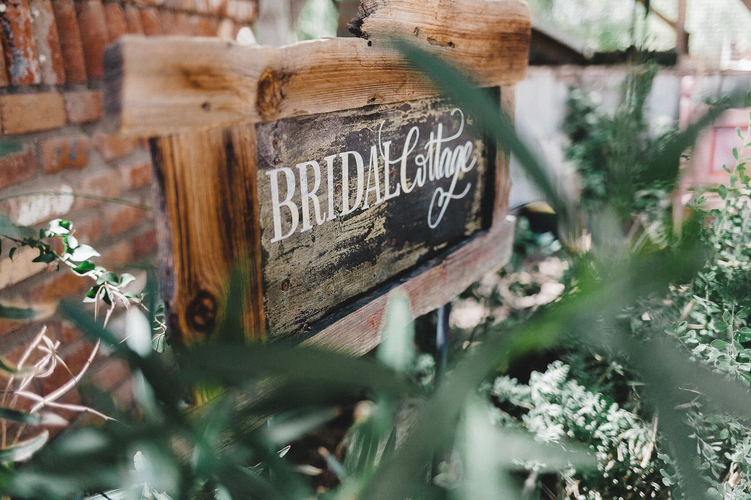 Rustic wooden Bridal Cottage sign surrounded by lush greenery at a wedding venue.