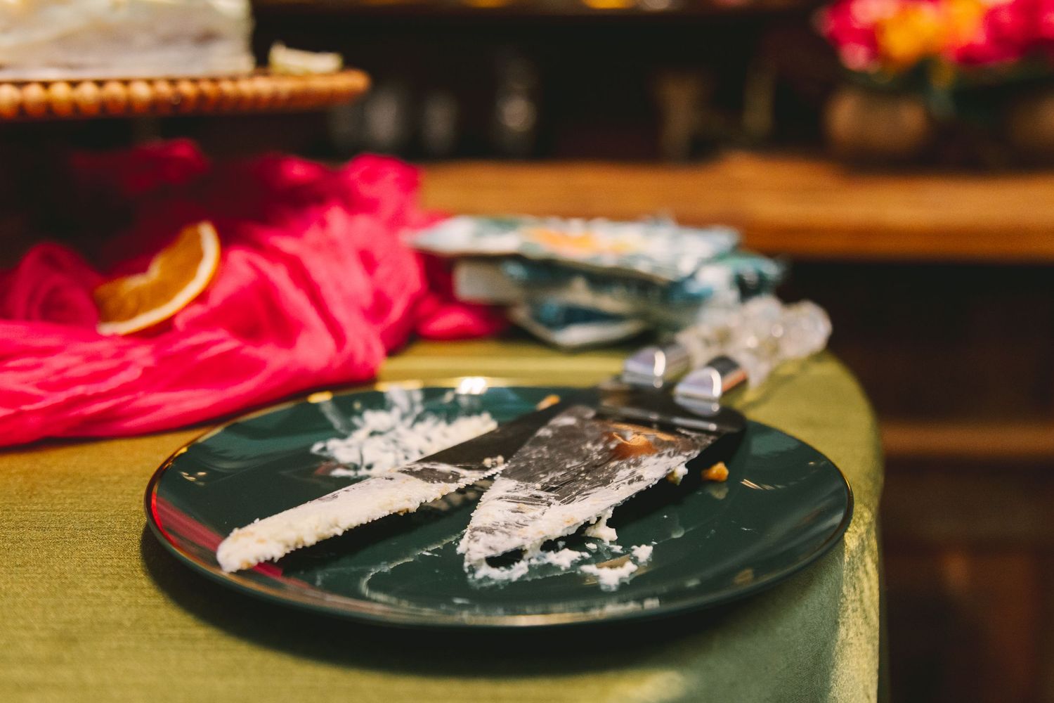 Slice of white cake on a dark green plate with a cake knife at an elegant event reception table.