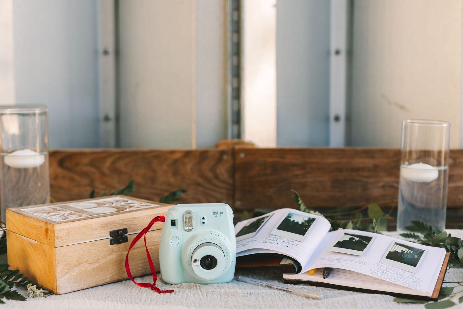 Instax mini camera, wooden keepsake box, and open photo album displayed on wedding guest book table.