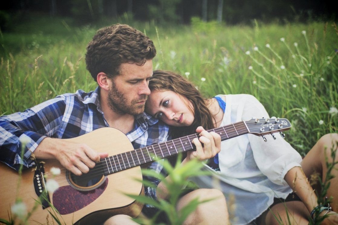 Romantic couple sitting in green meadow while man plays acoustic guitar for woman.
