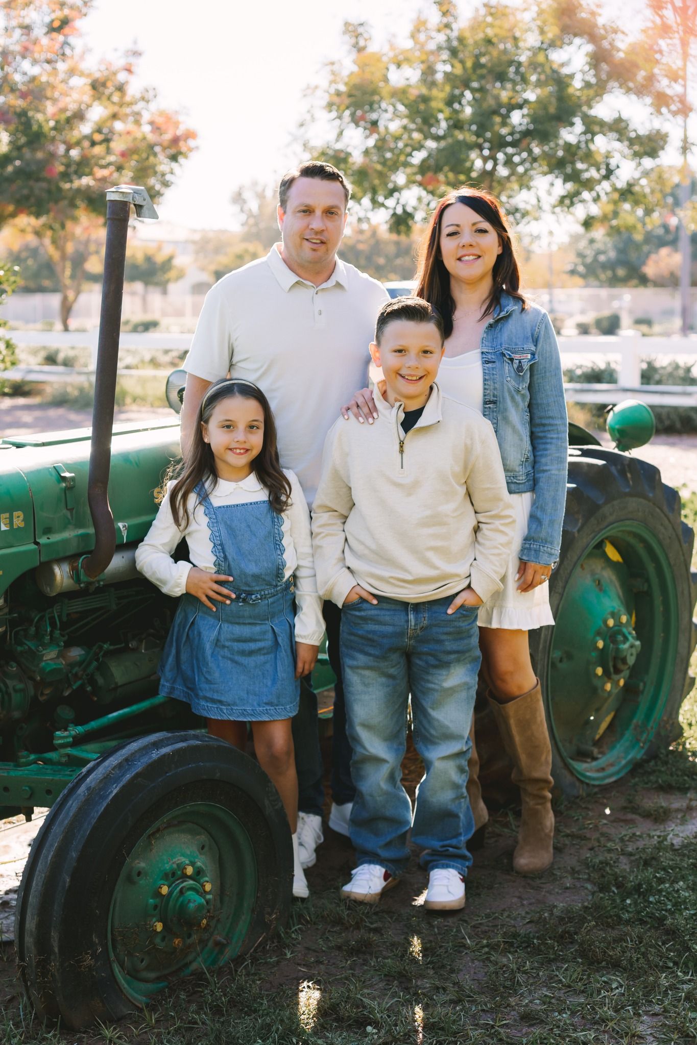 Smiling family of four posing beside vintage green tractor in autumn farm setting.