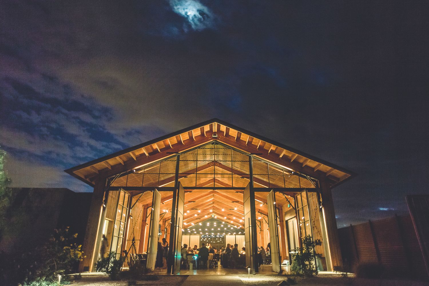 Stunning wedding venue glowing with warm lights against a dramatic night sky with moonlight.