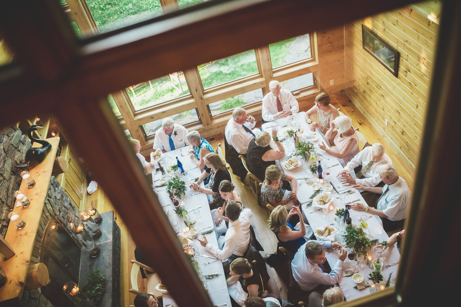 Aerial view of wedding reception guests seated at long decorated tables in wooden venue.