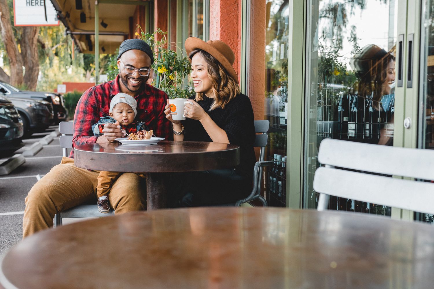 Young family with baby enjoying coffee at outdoor cafe.