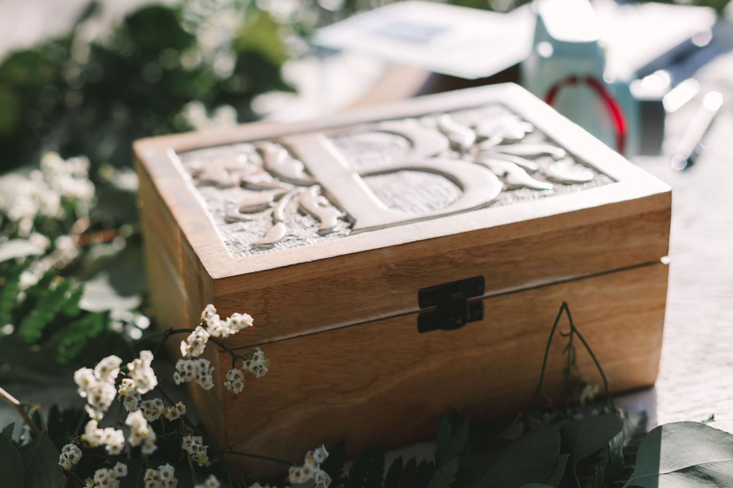 Decorative wooden keepsake box with carved tree design surrounded by white flowers and green foliage.