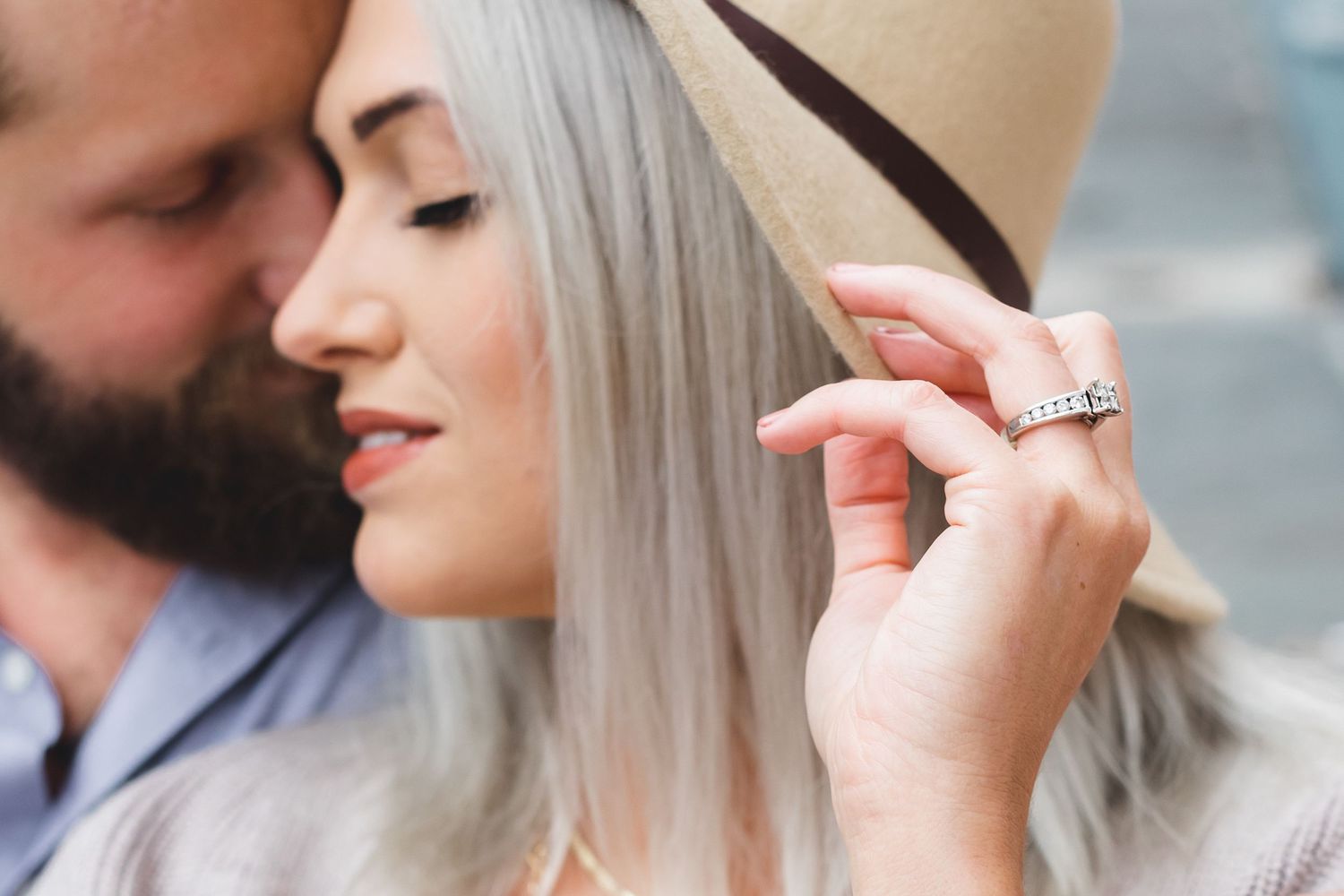 Close-up of woman with silver hair holding a hat brim while man kisses her cheek.