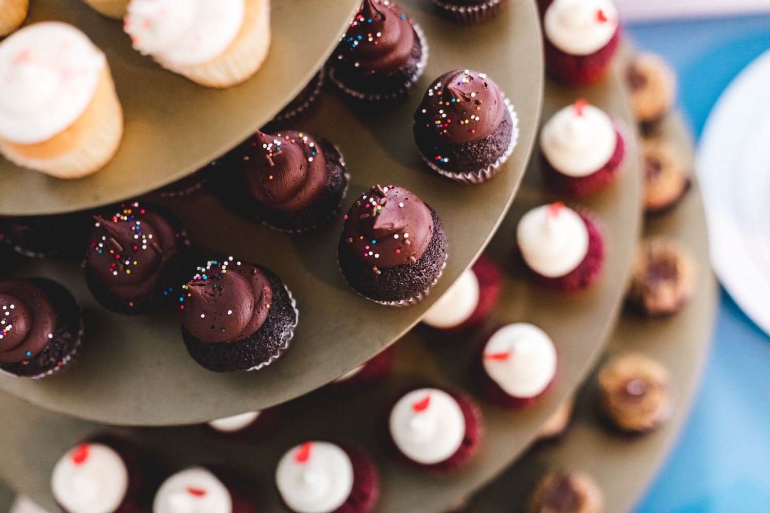 Three-tiered dessert stand displaying chocolate and vanilla frosted cupcakes with sprinkles at a wedding reception.