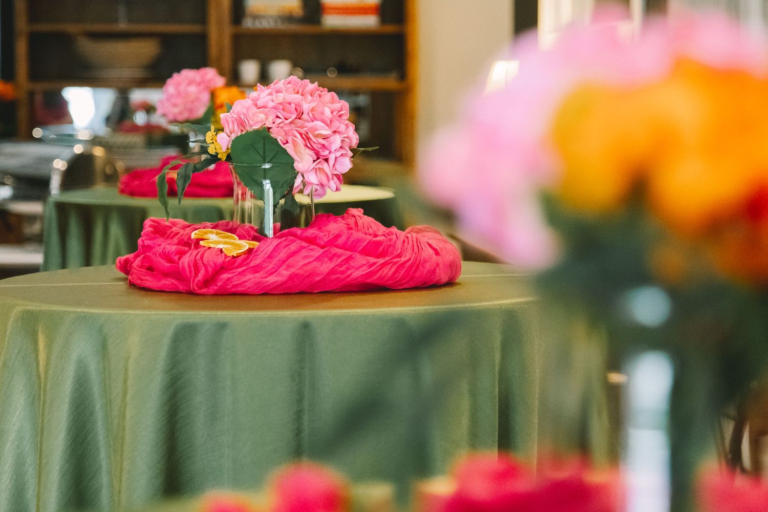 Elegant wedding reception tables with green linens and pink and orange floral centerpieces.
