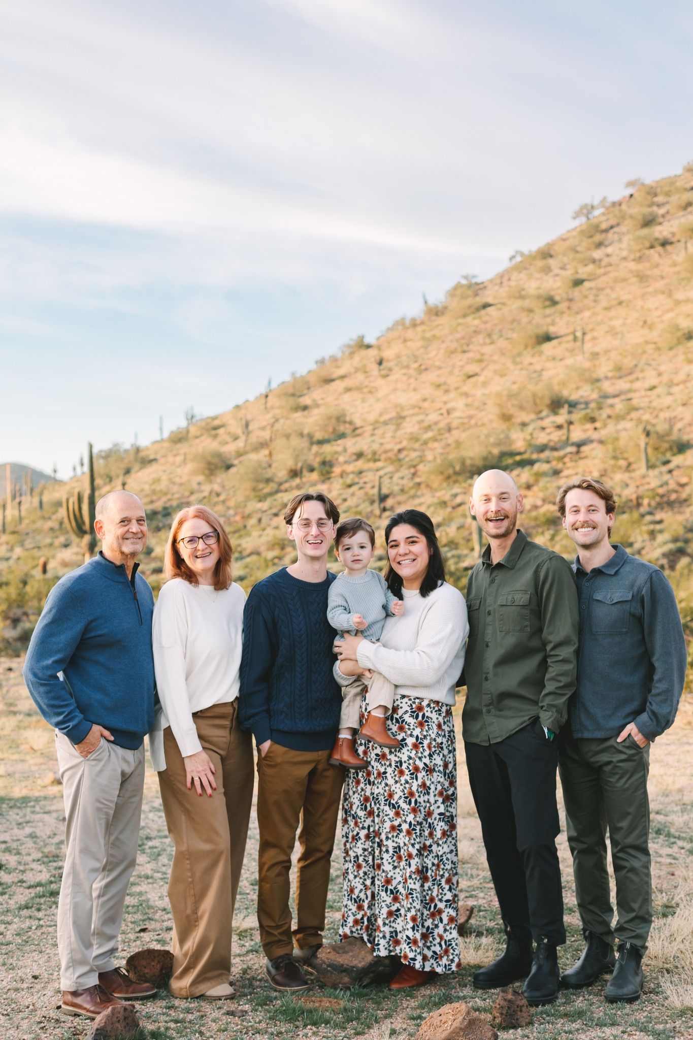 Extended family of seven posing together outdoors in a desert landscape with saguaro cacti.