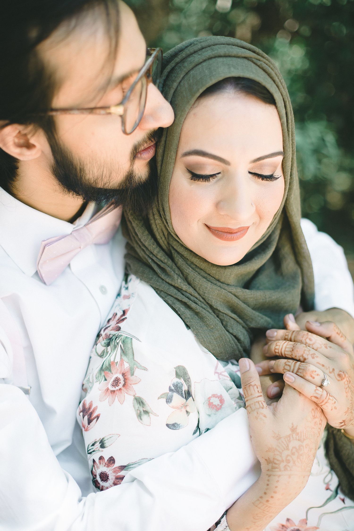 Romantic close-up of a couple, woman in green hijab with henna hands held by a bearded man in a white shirt.