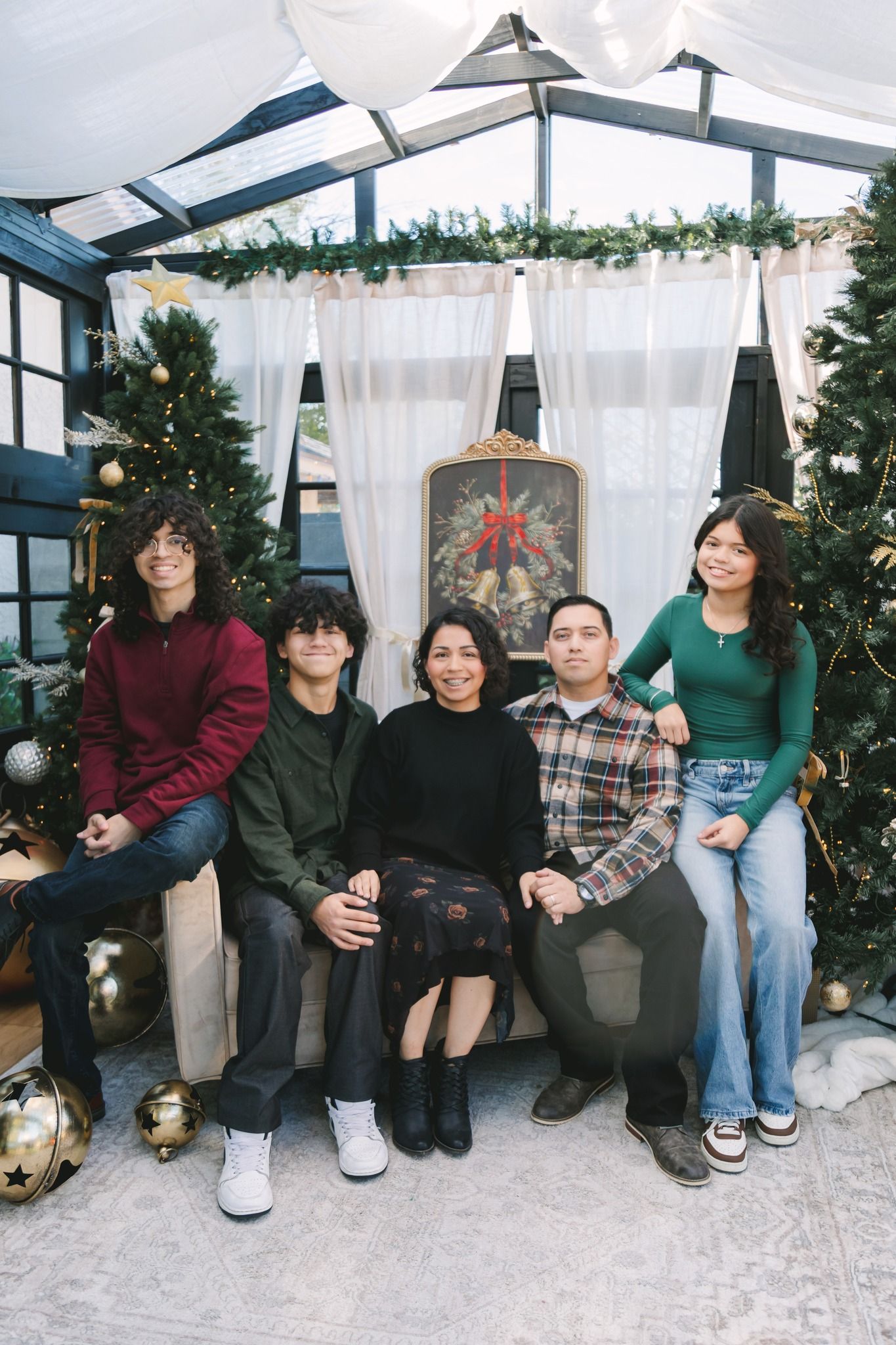 Latino family of five gathered around Christmas trees in festive holiday photo setting.