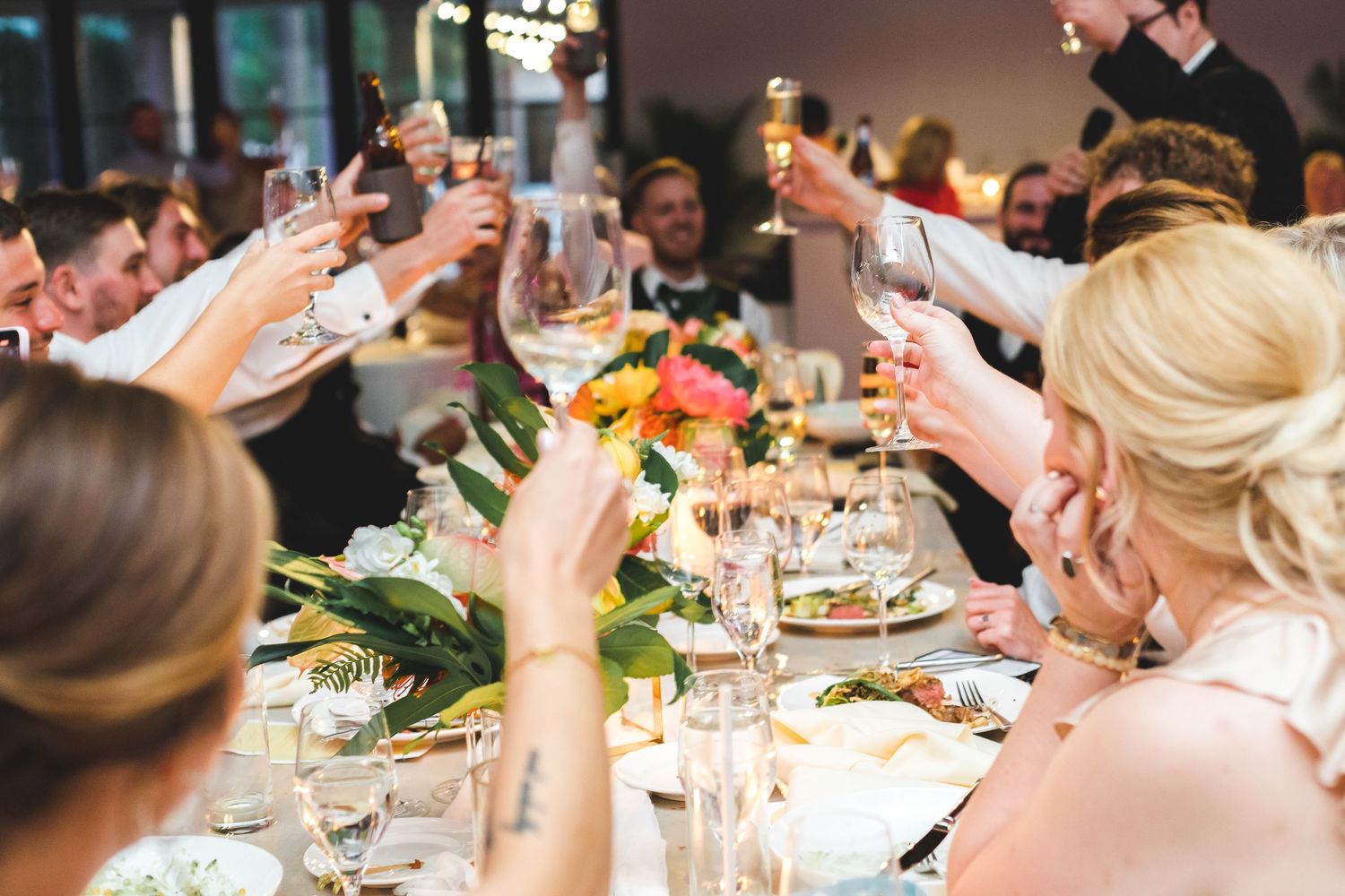 Wedding guests raise champagne glasses in a toast at elegantly decorated reception table.