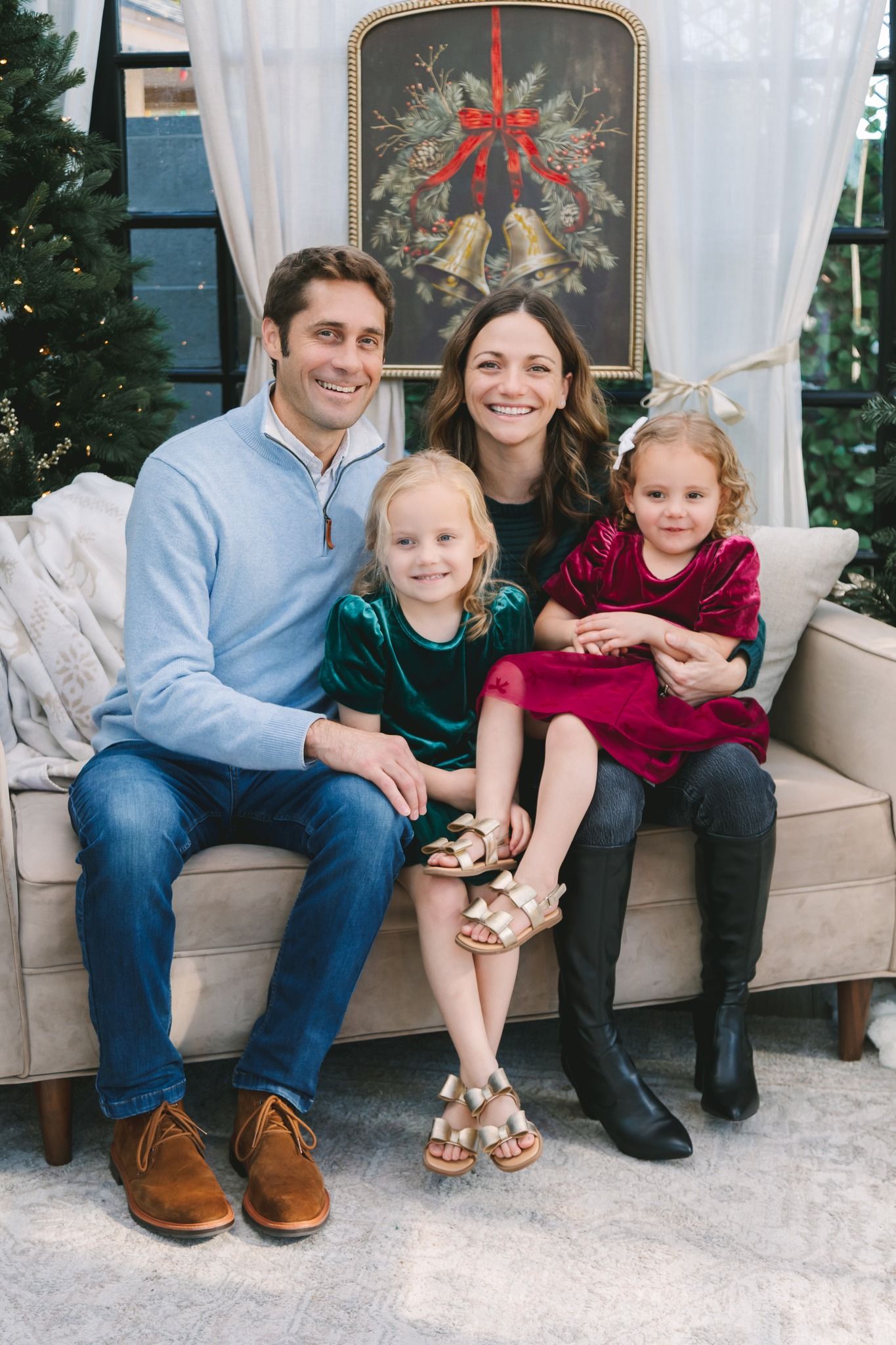 Family of four sitting on a couch in a festive holiday decorated room with Christmas trees.