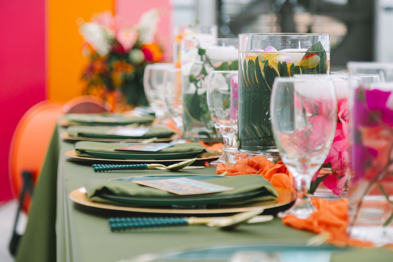 Green and orange wedding reception table setting with glassware and colorful centerpieces.