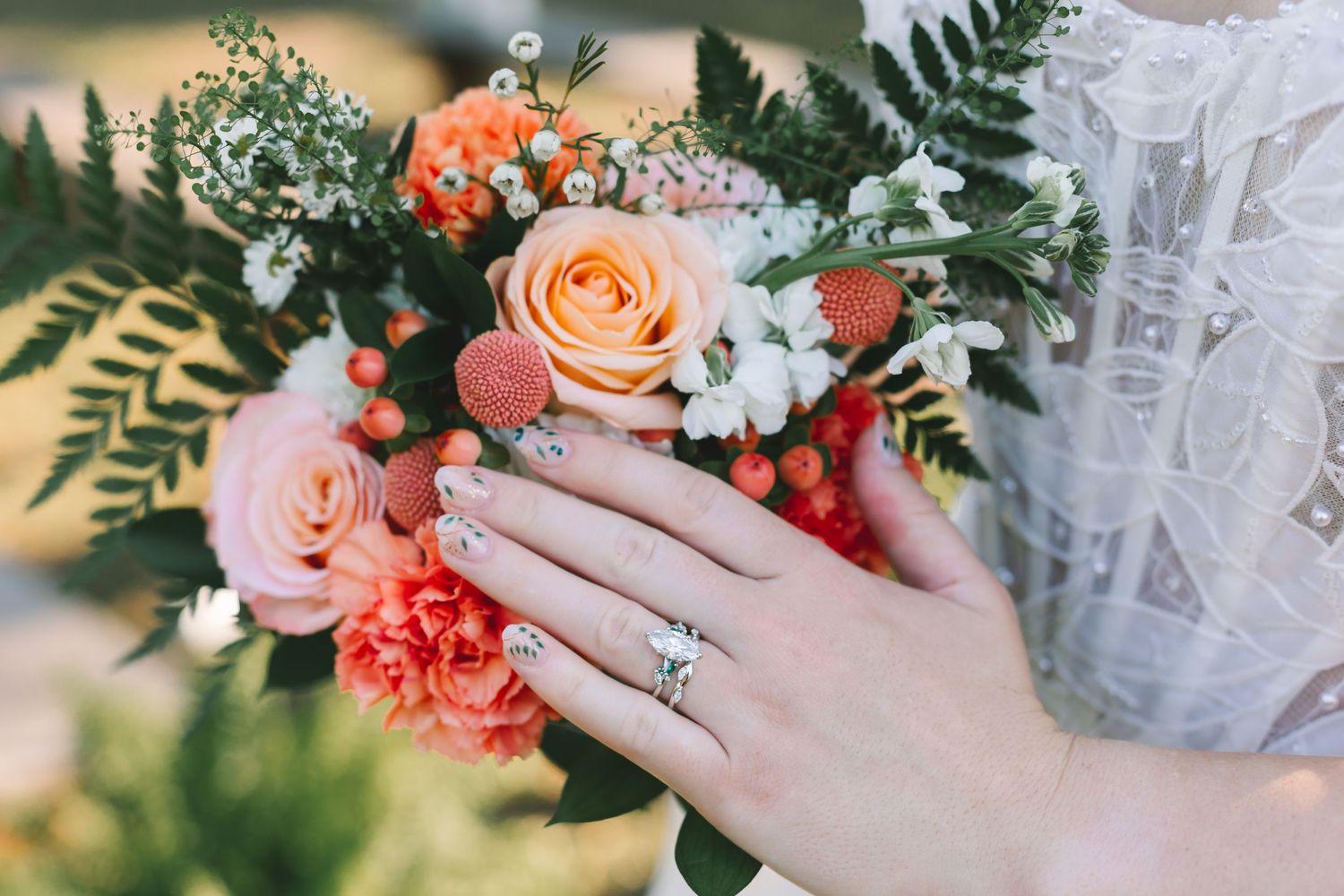 Close-up of bride's hand displaying diamond engagement ring while holding a peach and coral wedding bouquet.