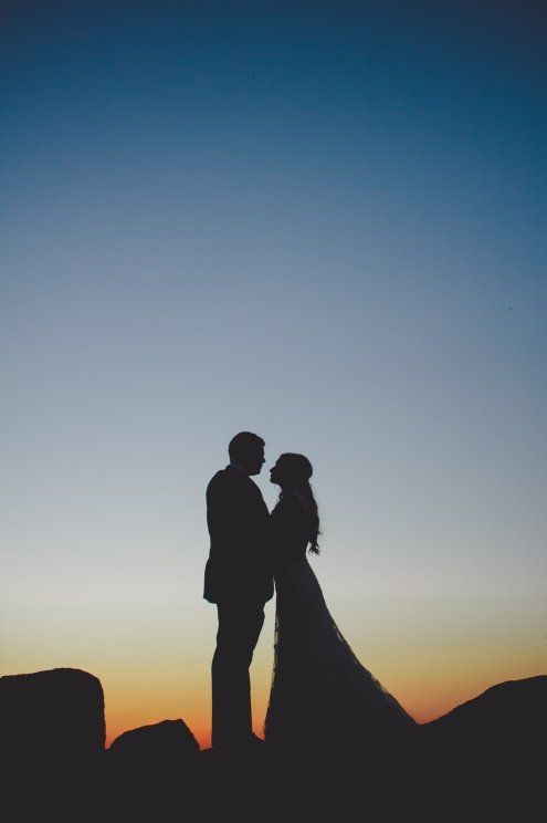 Romantic silhouette of bride and groom embracing against a stunning sunset sky.