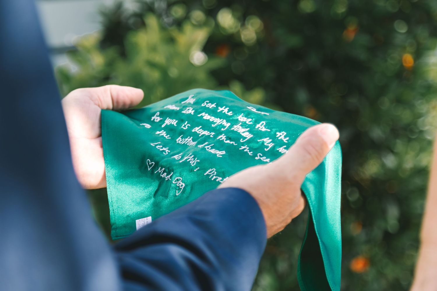 Groom holds green handkerchief with handwritten personal vows message at outdoor wedding.