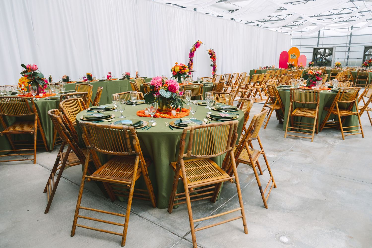 Elegant wedding reception with green tablecloths, bamboo chairs, and colorful floral centerpieces in greenhouse venue.