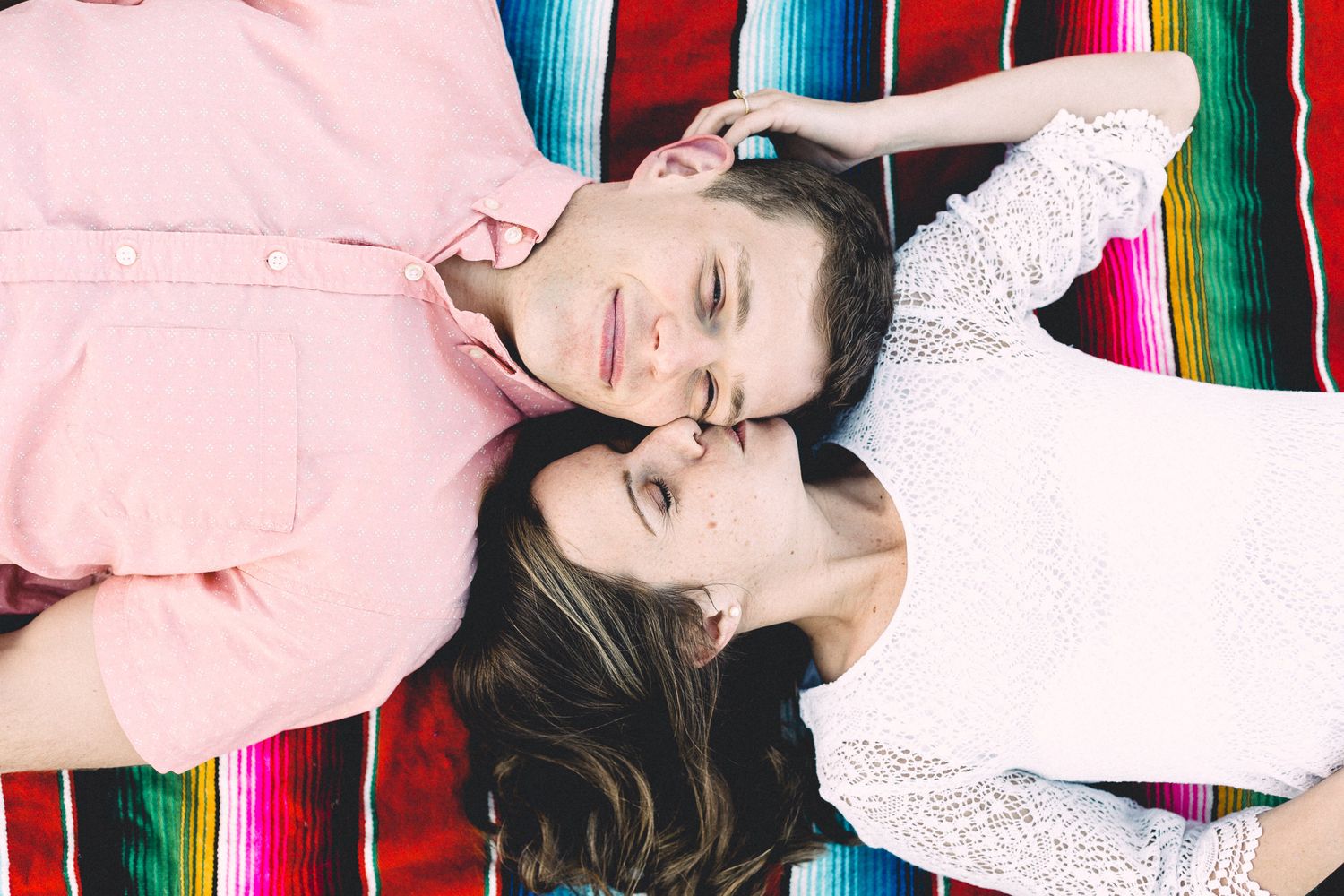 Couple lying head-to-head on a colorful striped blanket with eyes closed in a peaceful, intimate moment.