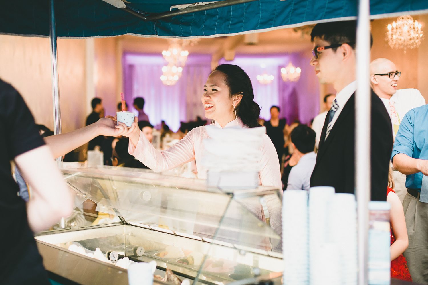 Smiling bride in white dress served at a food station during her wedding reception.