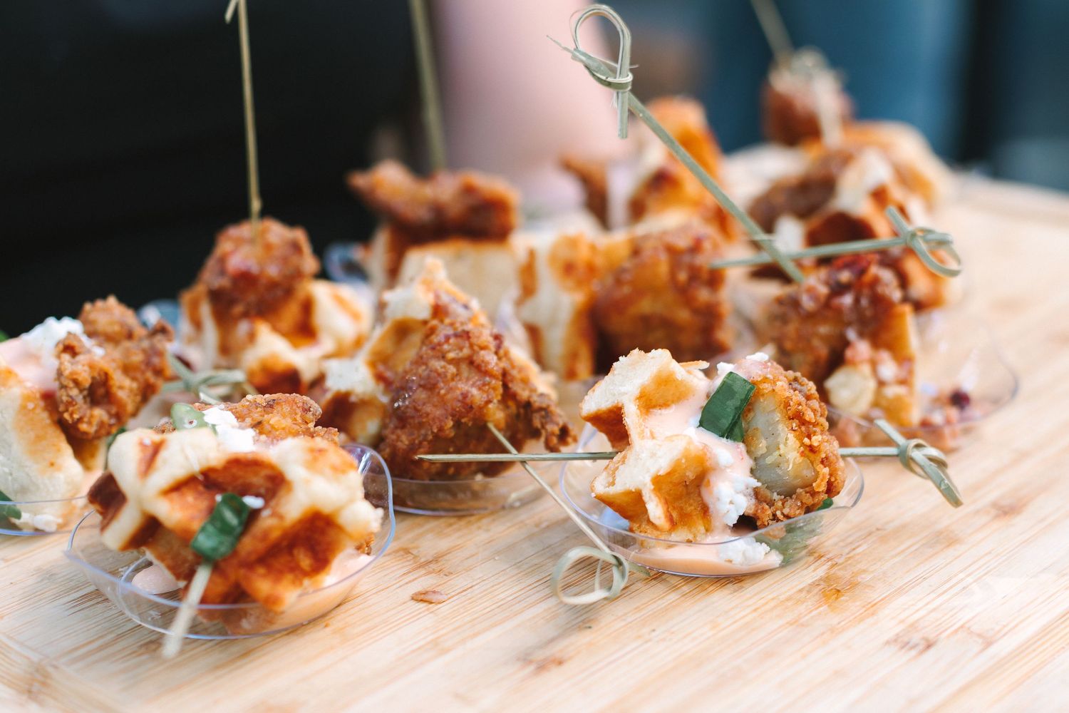 Crispy fried chicken appetizers served on mini waffles displayed on wooden board at wedding reception.