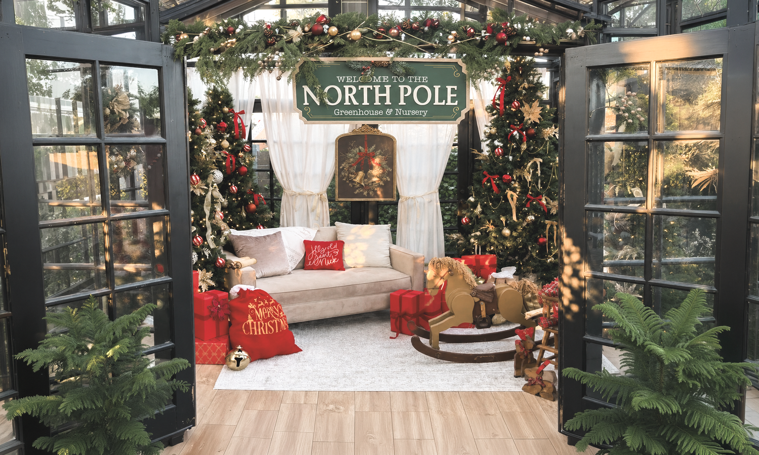 Festive North Pole Christmas display with decorated trees, gifts, and cozy seating in a greenhouse-style holiday setting.