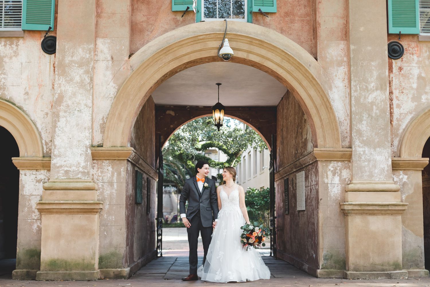 Bride and groom standing under historic stone archway with hanging lantern on wedding day.