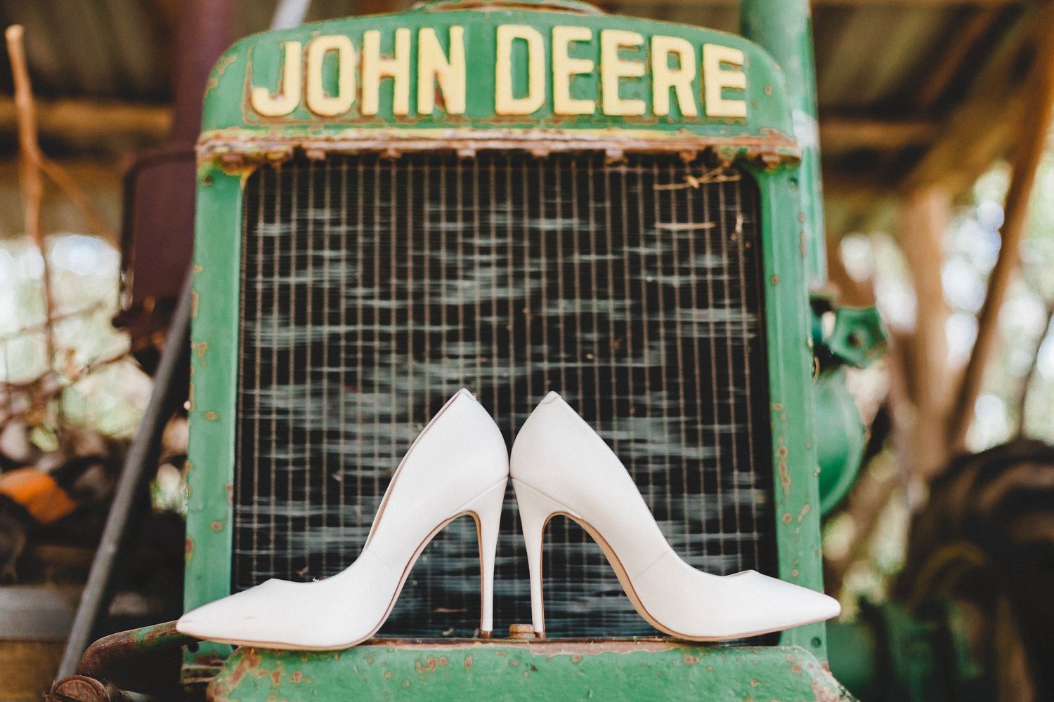 White bridal heels displayed on the front of a vintage green John Deere tractor.