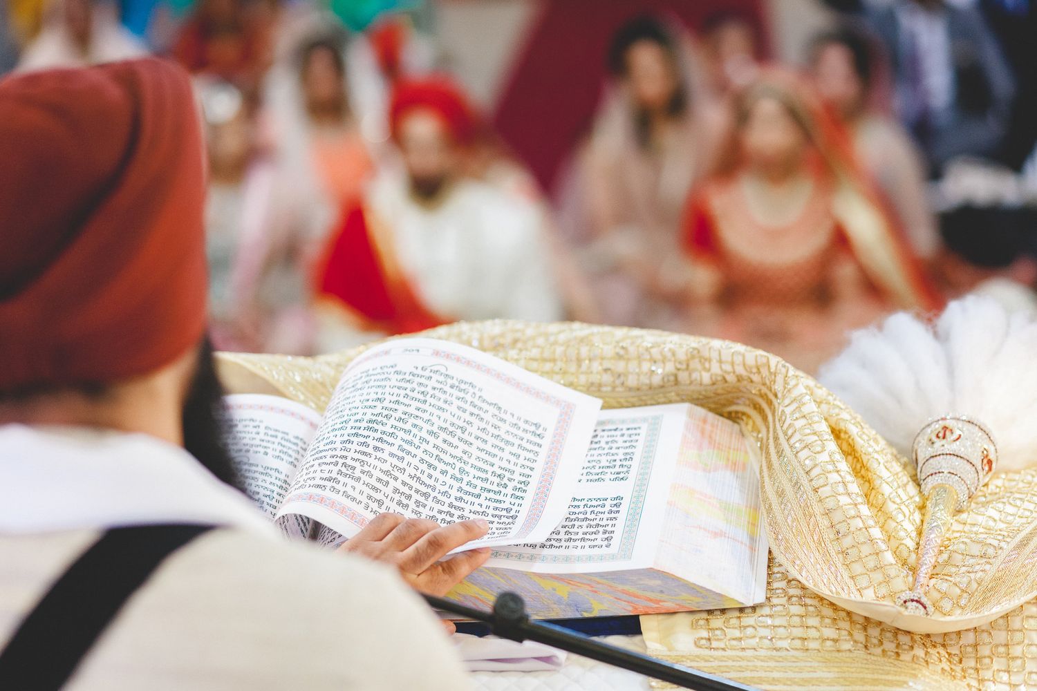 Sikh priest reading from Guru Granth Sahib during traditional Anand Karaj wedding ceremony.