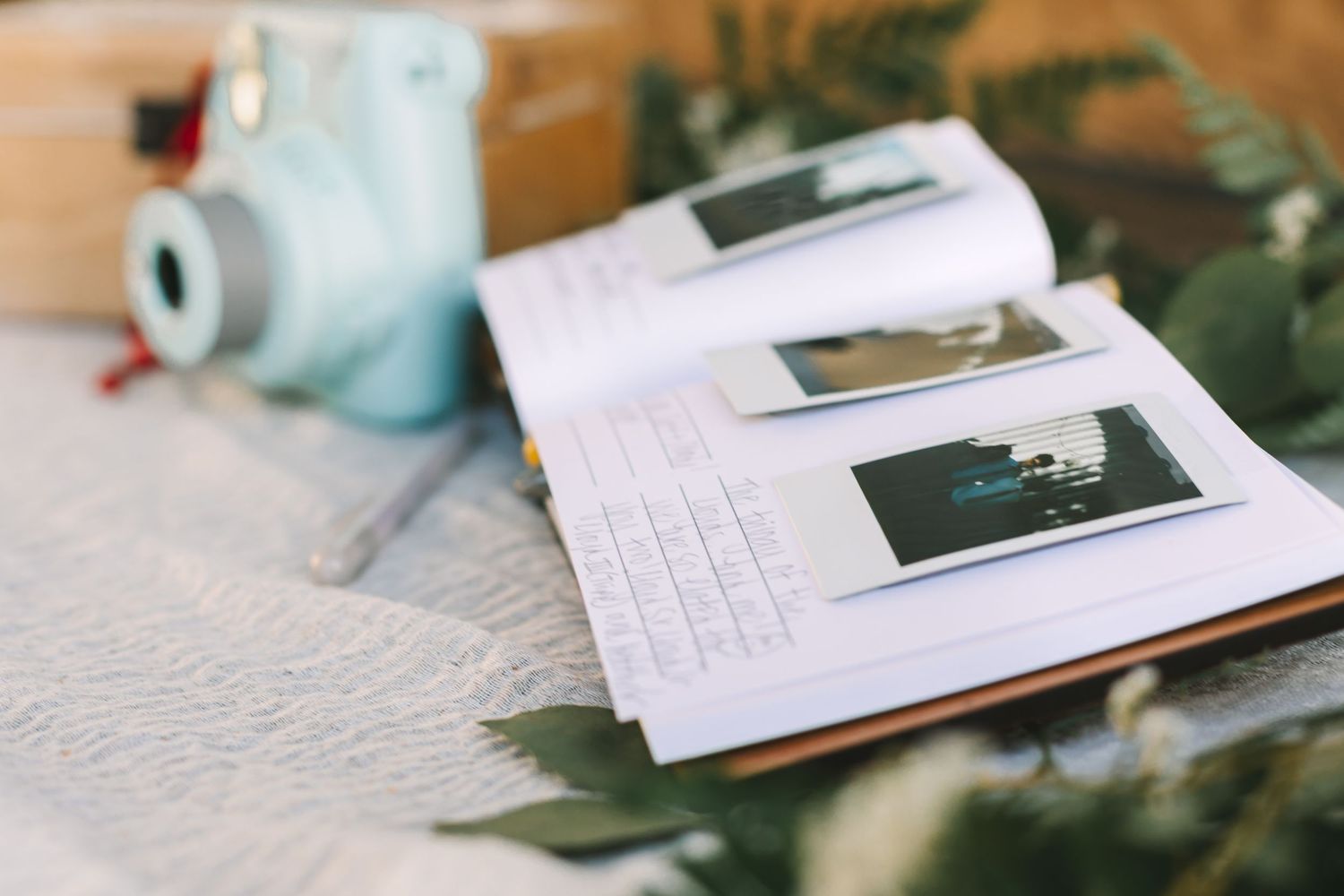 Wedding guest book with Polaroid photos and handwritten notes displayed beside a mint Instax camera.