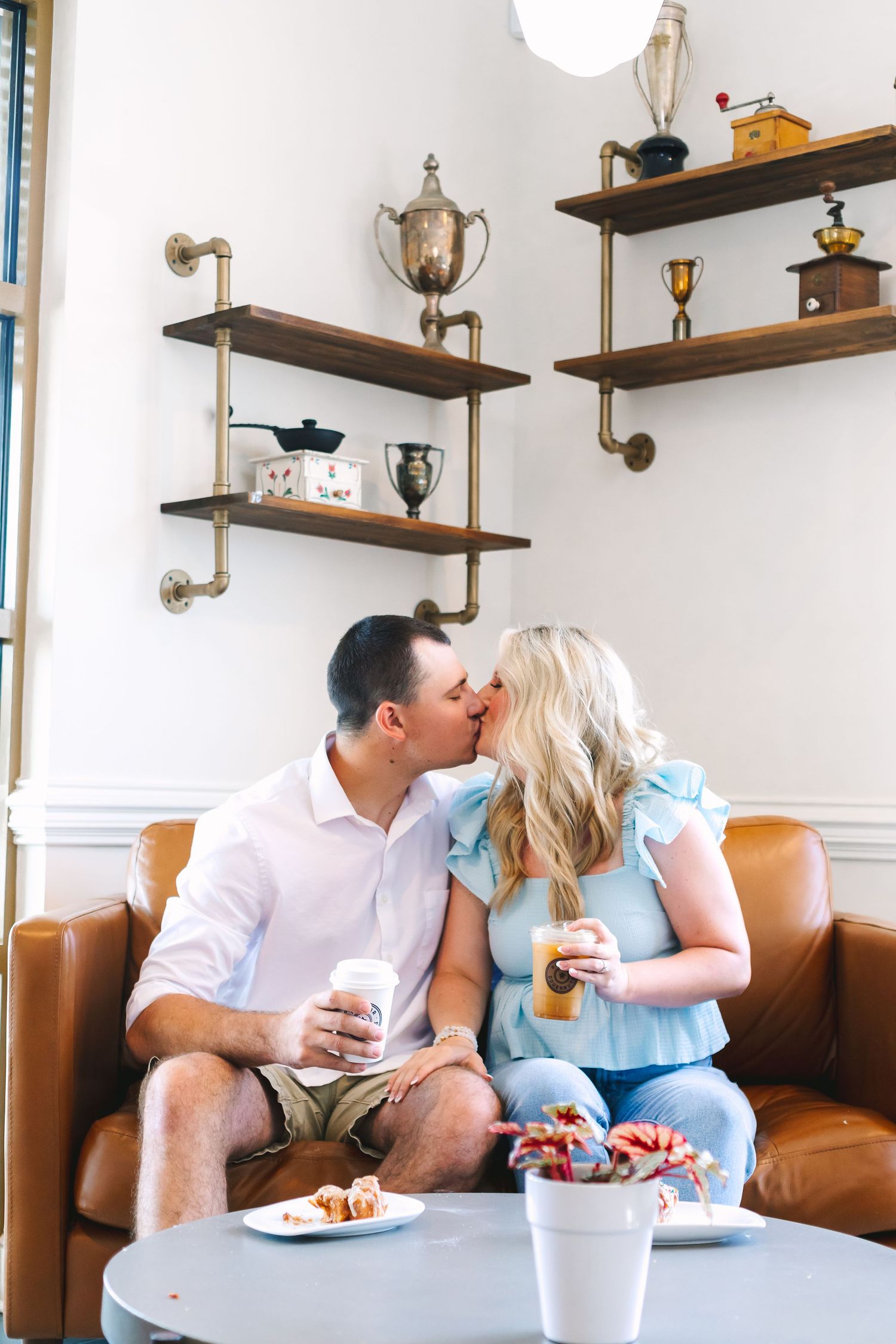 Couple kissing on a leather sofa while holding coffee cups in a cozy cafe.