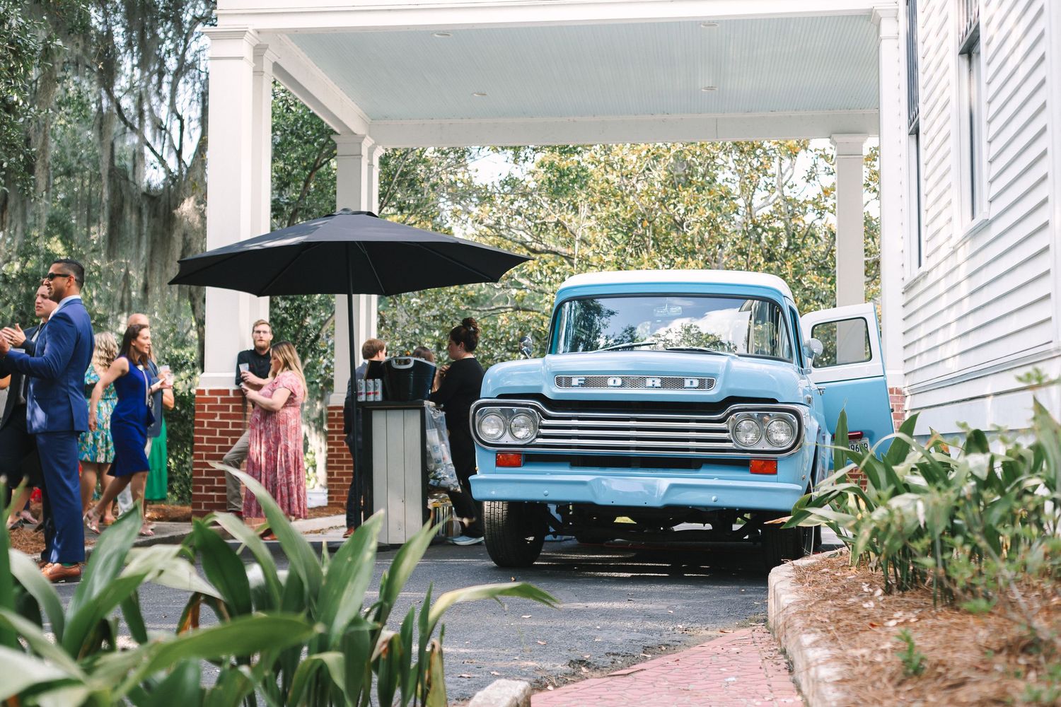 Vintage blue Ford truck parked outside wedding venue with guests mingling in background.