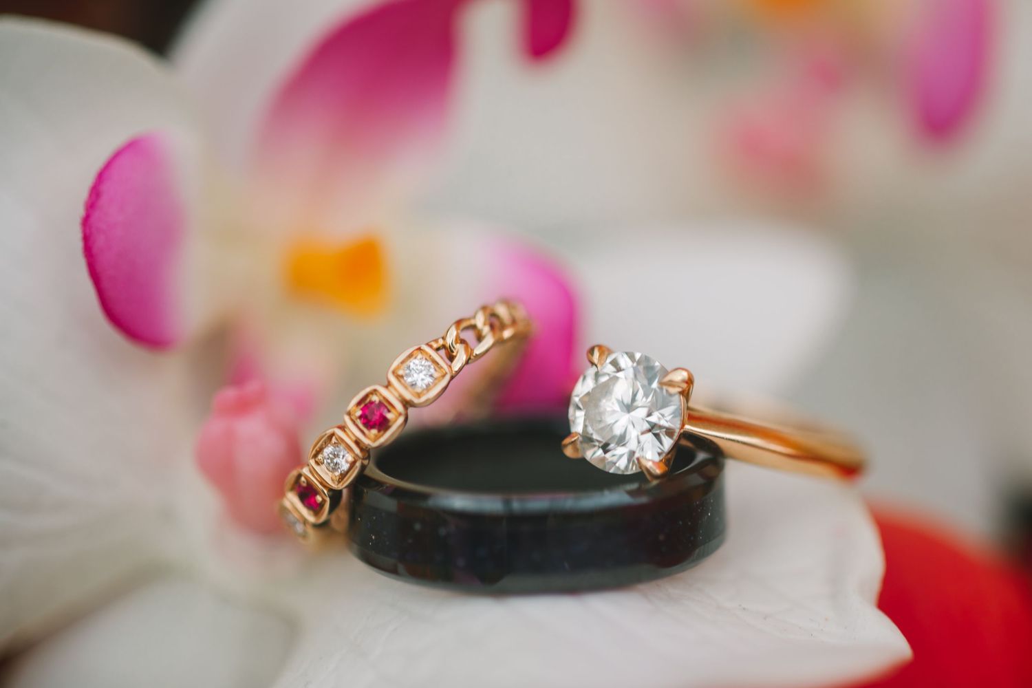 Gold engagement ring with round diamond and ruby eternity band resting on orchid flower.