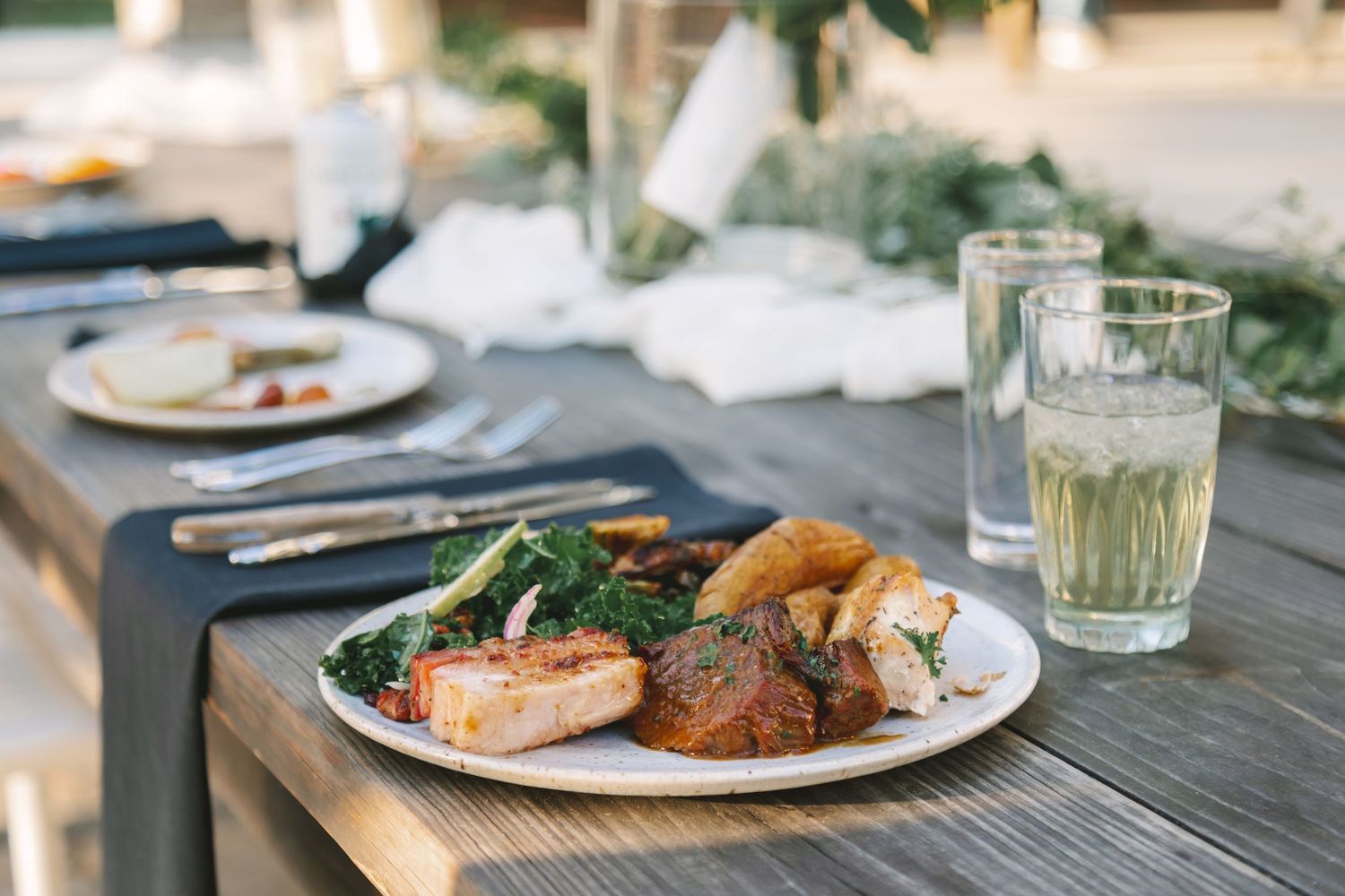 Elegant wedding reception dinner plate with salmon, roasted vegetables, and greens served on rustic wood table.
