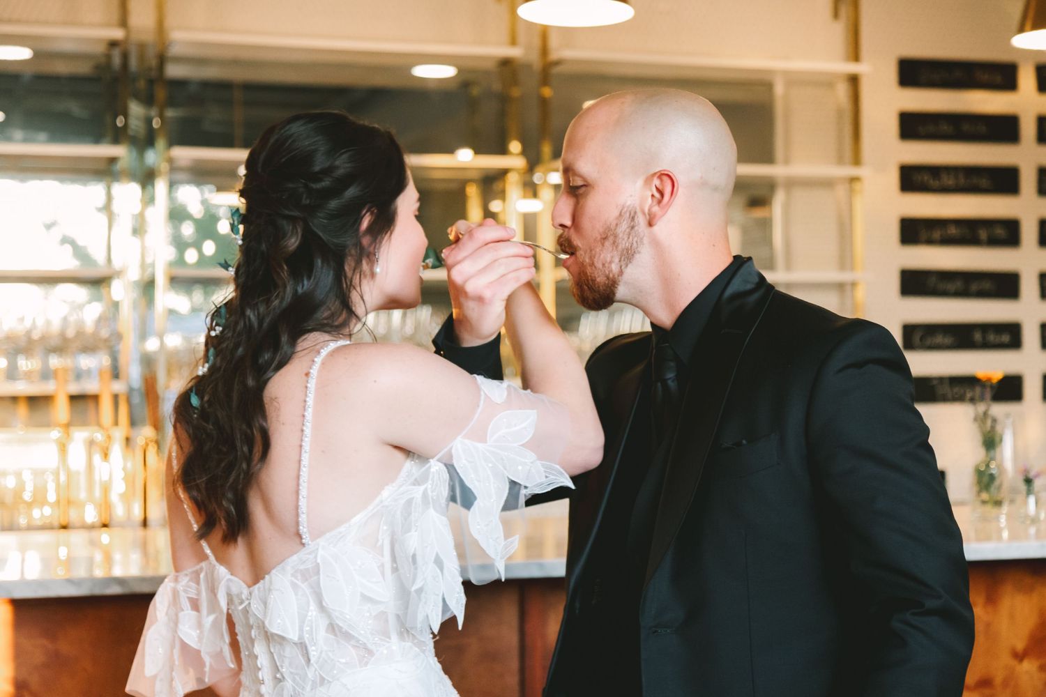 Groom in black suit tenderly kisses bride's hand during romantic first dance at wedding reception.