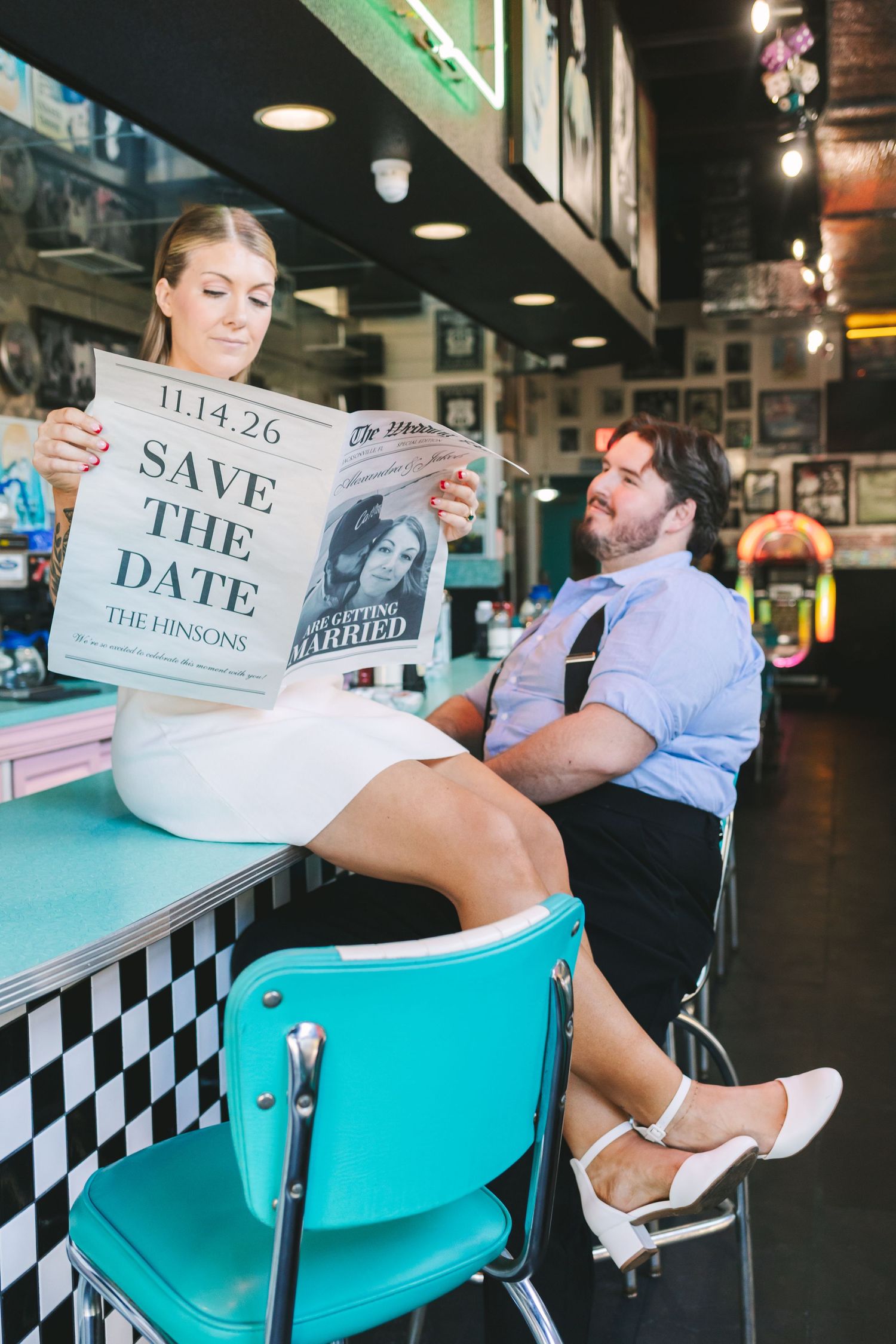 Couple at retro diner counter reading Save the Date newspaper announcement for The Hinsons wedding on 11.14.26.