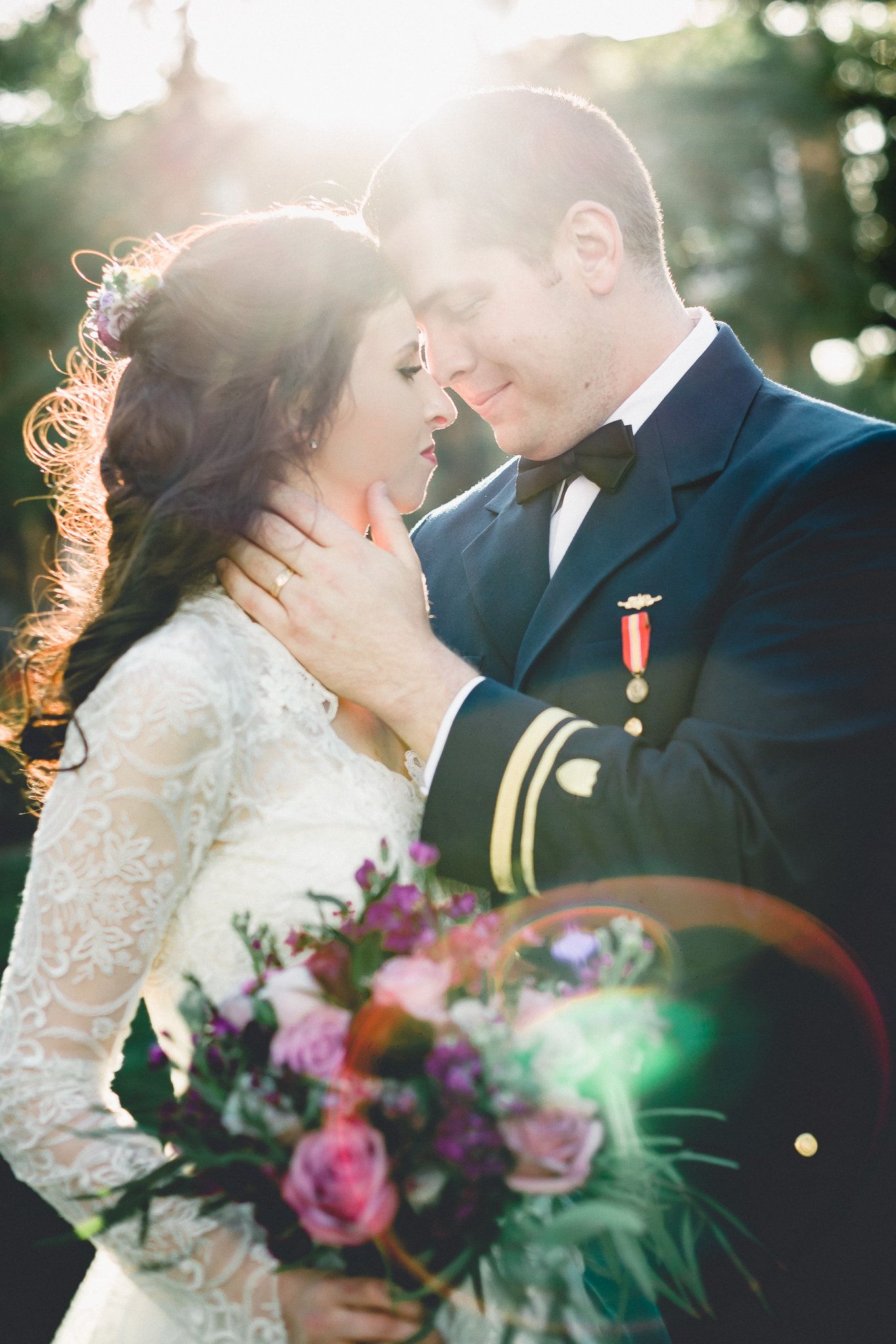Romantic couple in military wedding attire embracing in golden sunlight with floral bouquet.