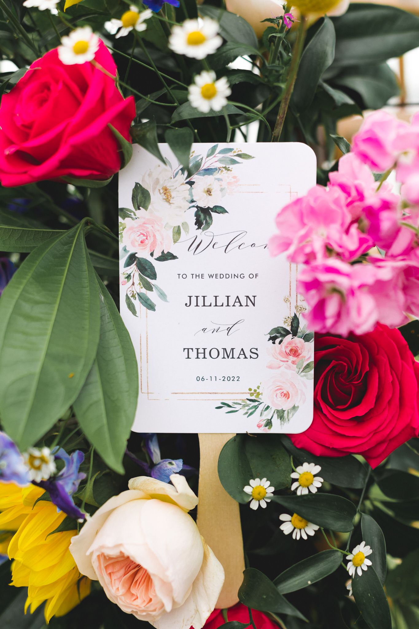 Colorful floral wedding welcome sign for Jillian and Thomas dated 06-11-2022 surrounded by vibrant roses and daisies.